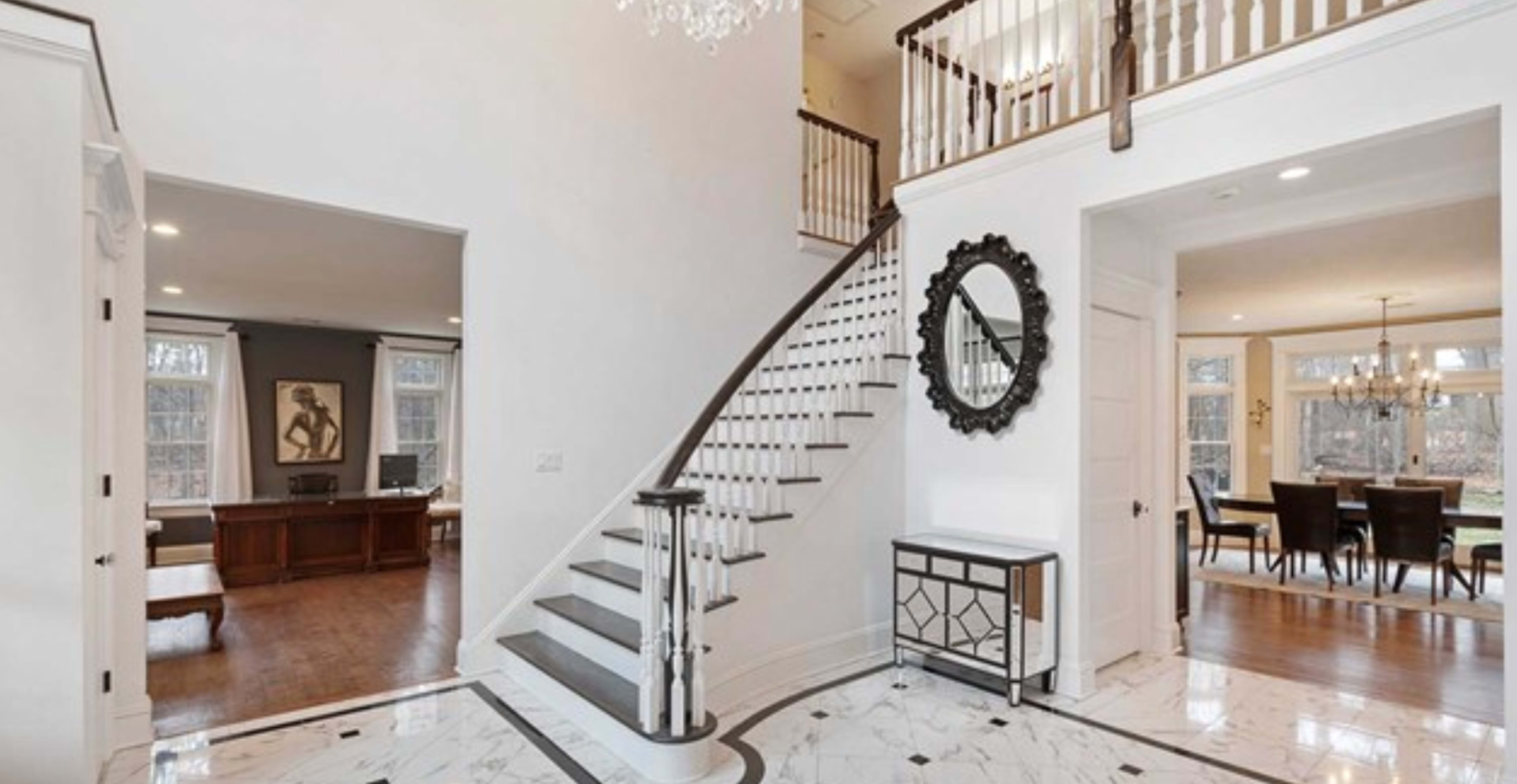 A foyer with a staircase leading to an upper level, framed by a large mirror and featuring a marble floor.