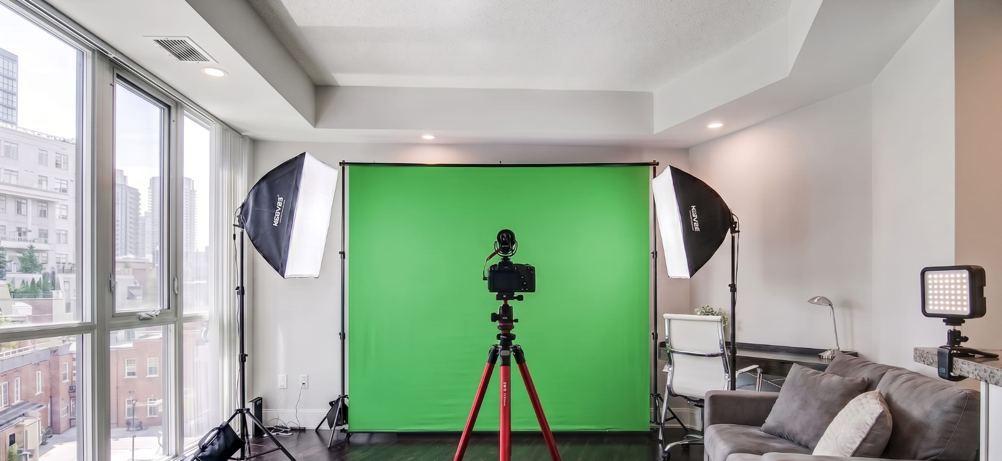 A photography setup featuring a green backdrop with a camera on a tripod and bright lighting equipment in a contemporary living space.