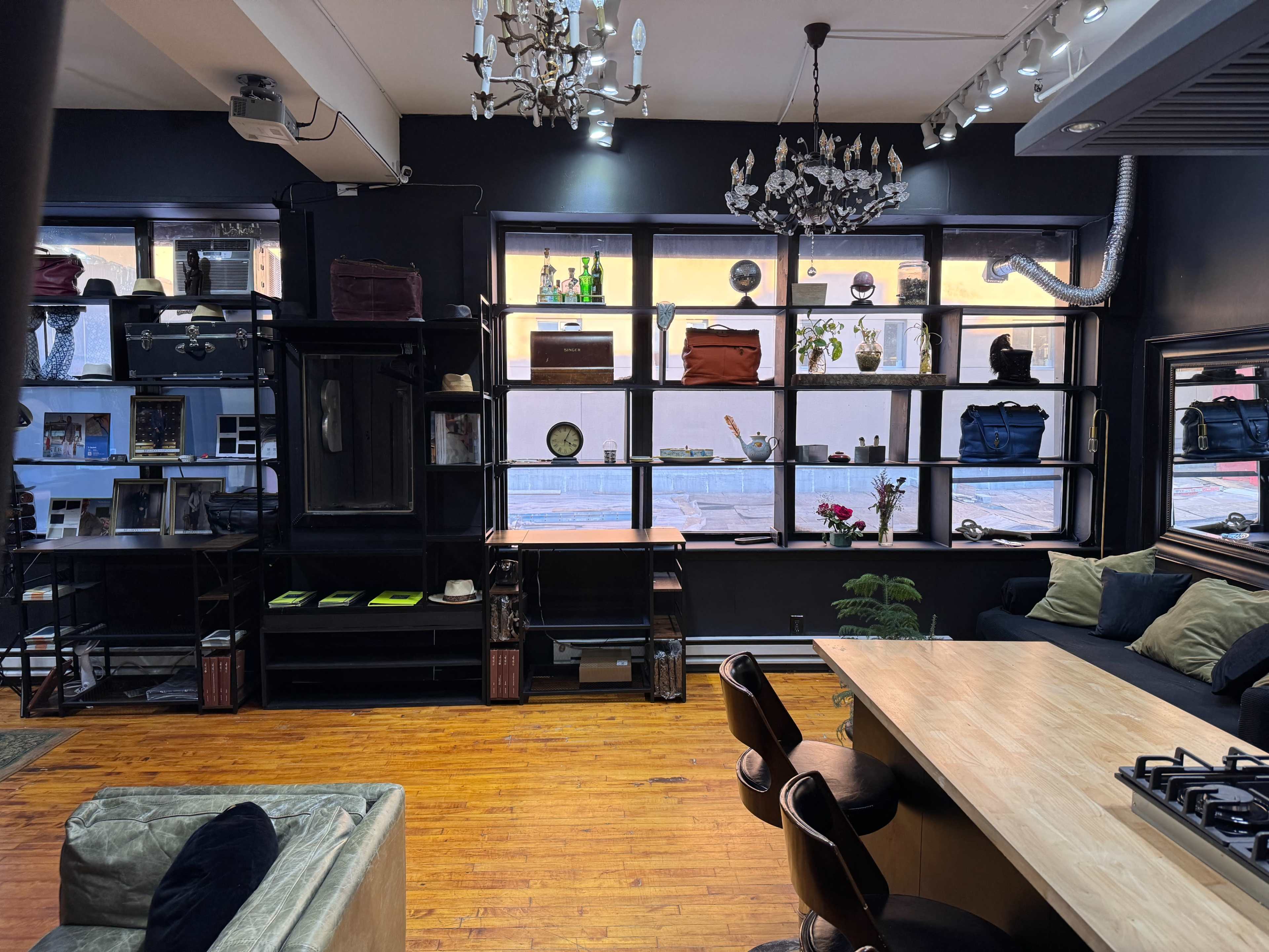 A cozy interior features a wooden countertop, black shelves filled with various items, and large windows displaying the street outside.