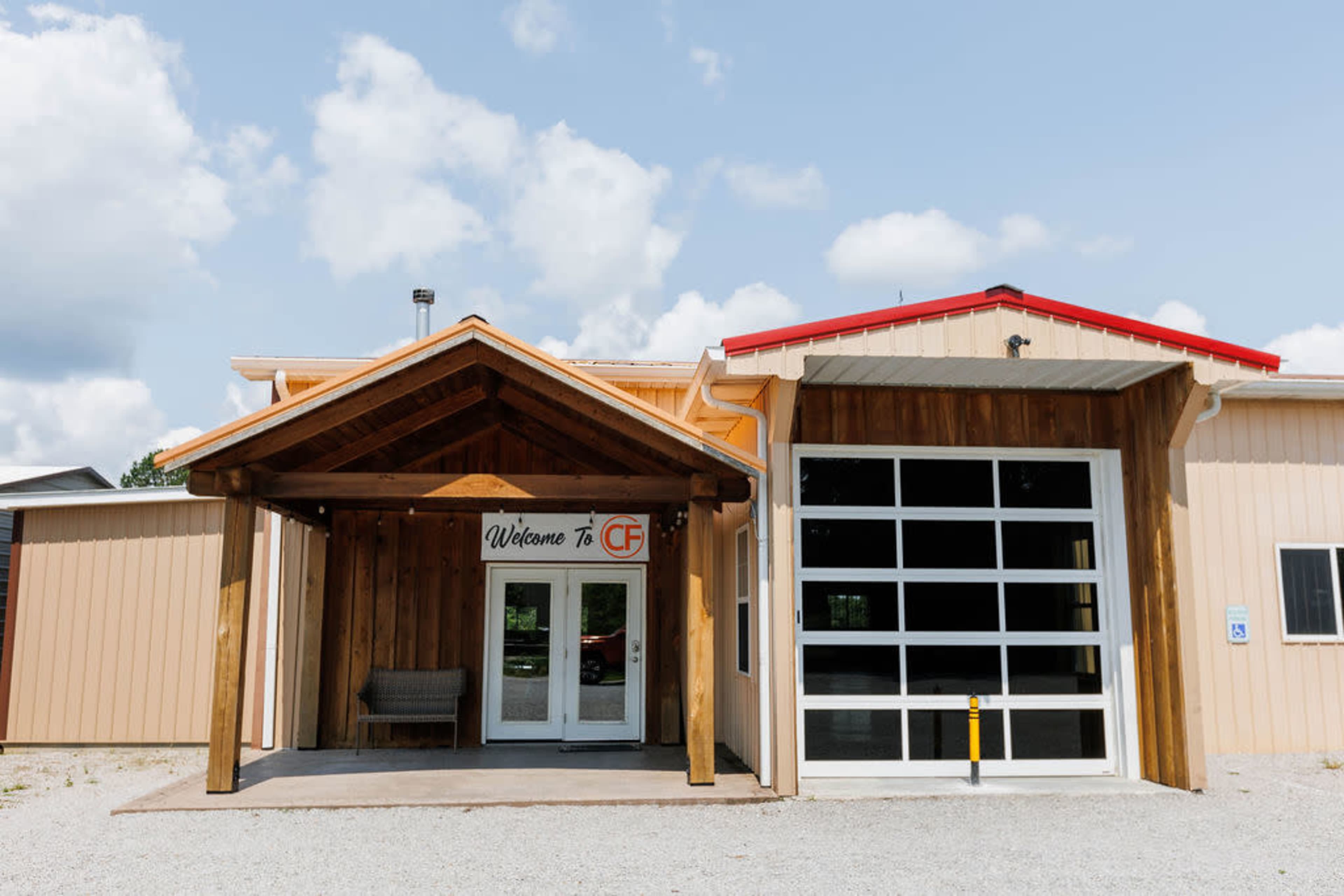 The image shows a building entrance featuring a wooden awning, a glass double door with a welcome sign, and a large garage-style door to the right.
