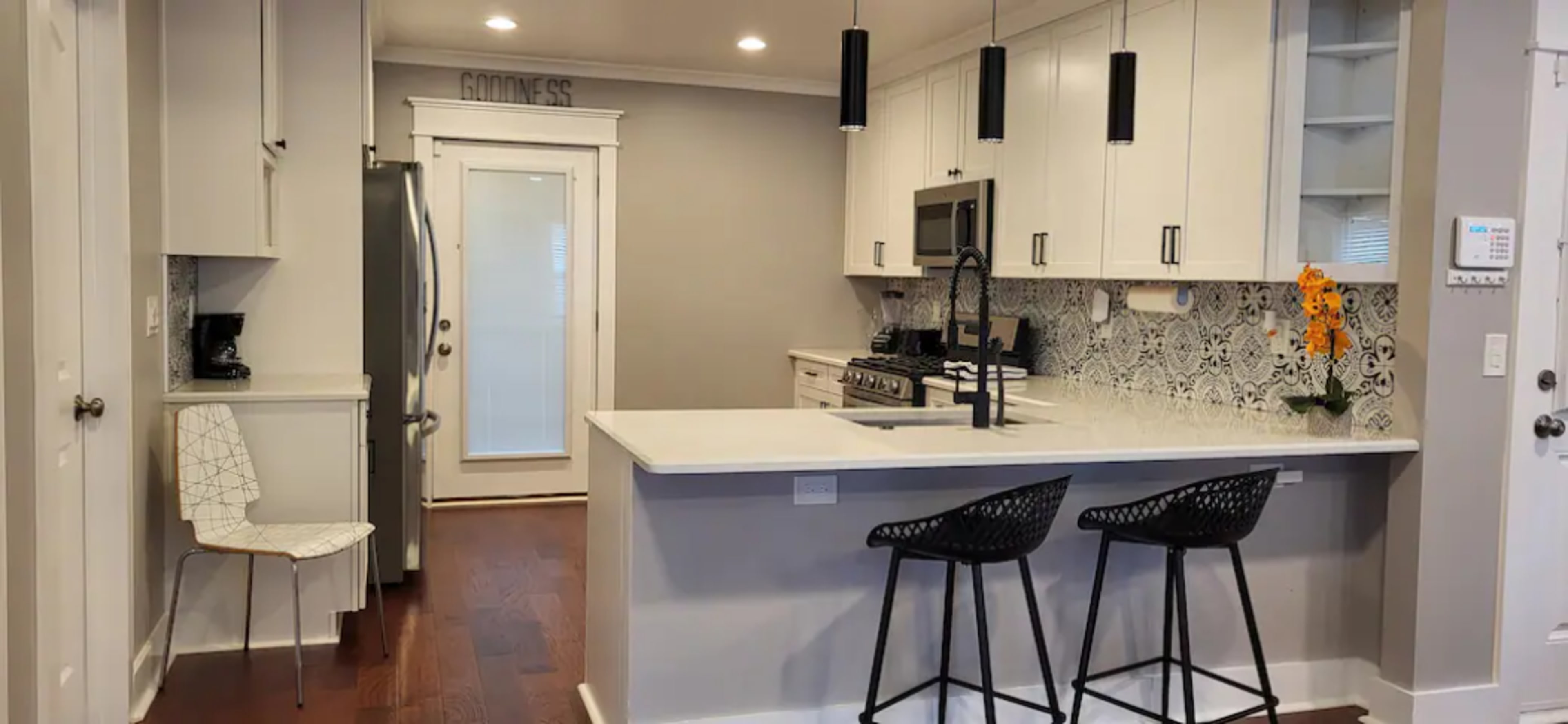 A modern kitchen features white cabinetry, stainless steel appliances, and a center island with two black bar stools.