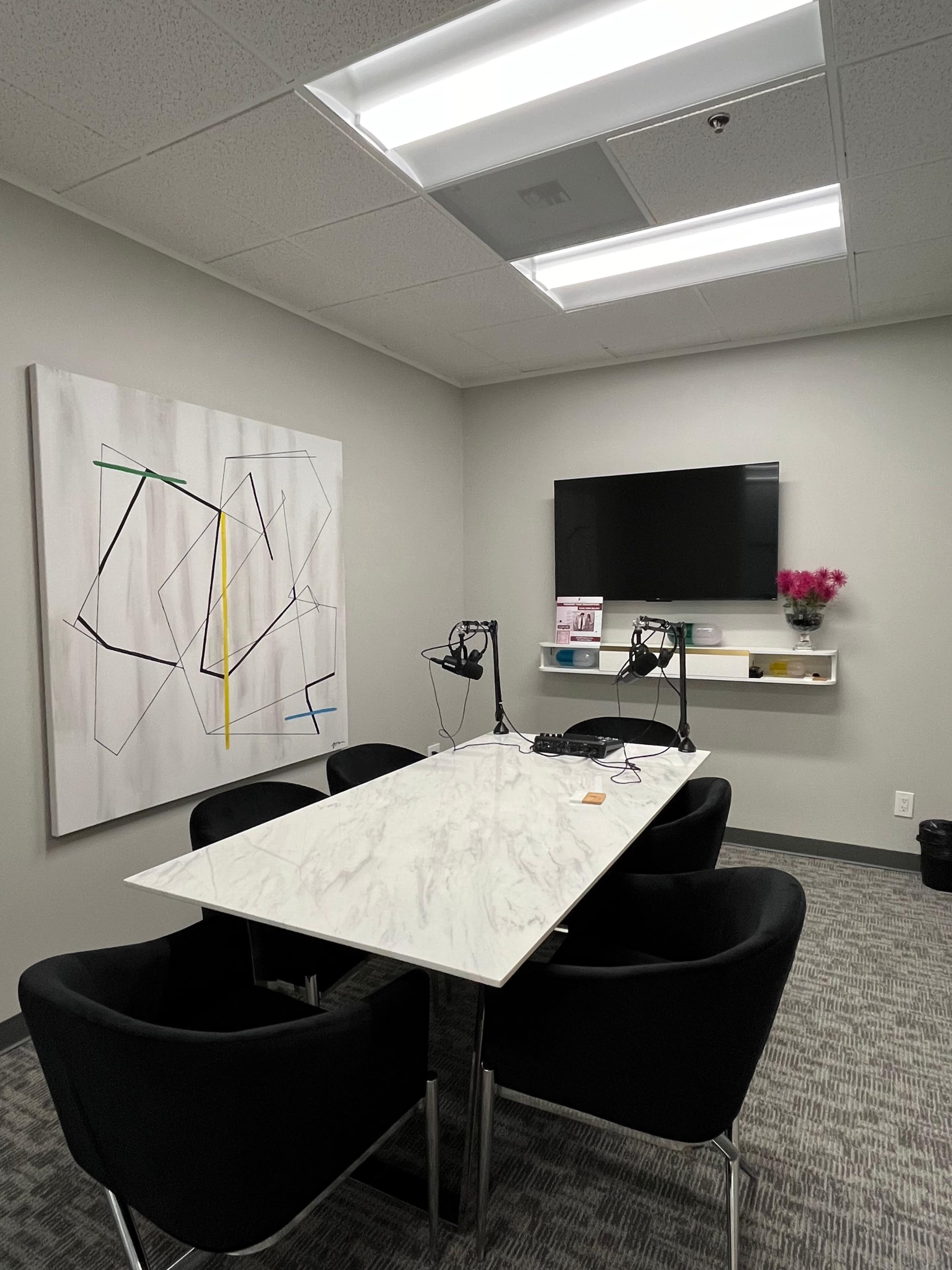 A modern conference room features a marble table surrounded by black chairs, a mounted television, and a large abstract painting on the wall.