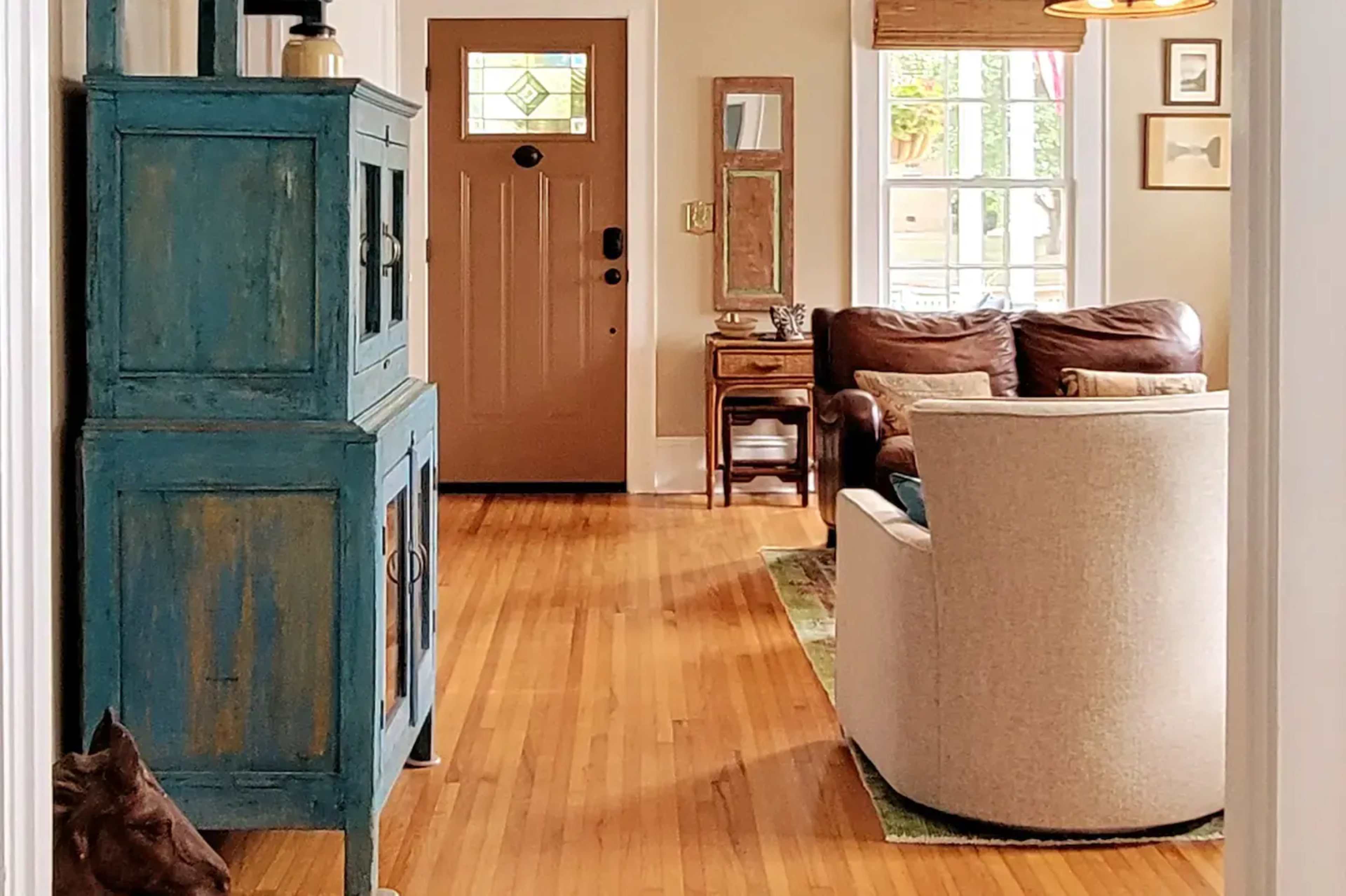 A light-filled hallway leading to a brown front door, with a blue cabinet on the left and a brown leather sofa on the right.
