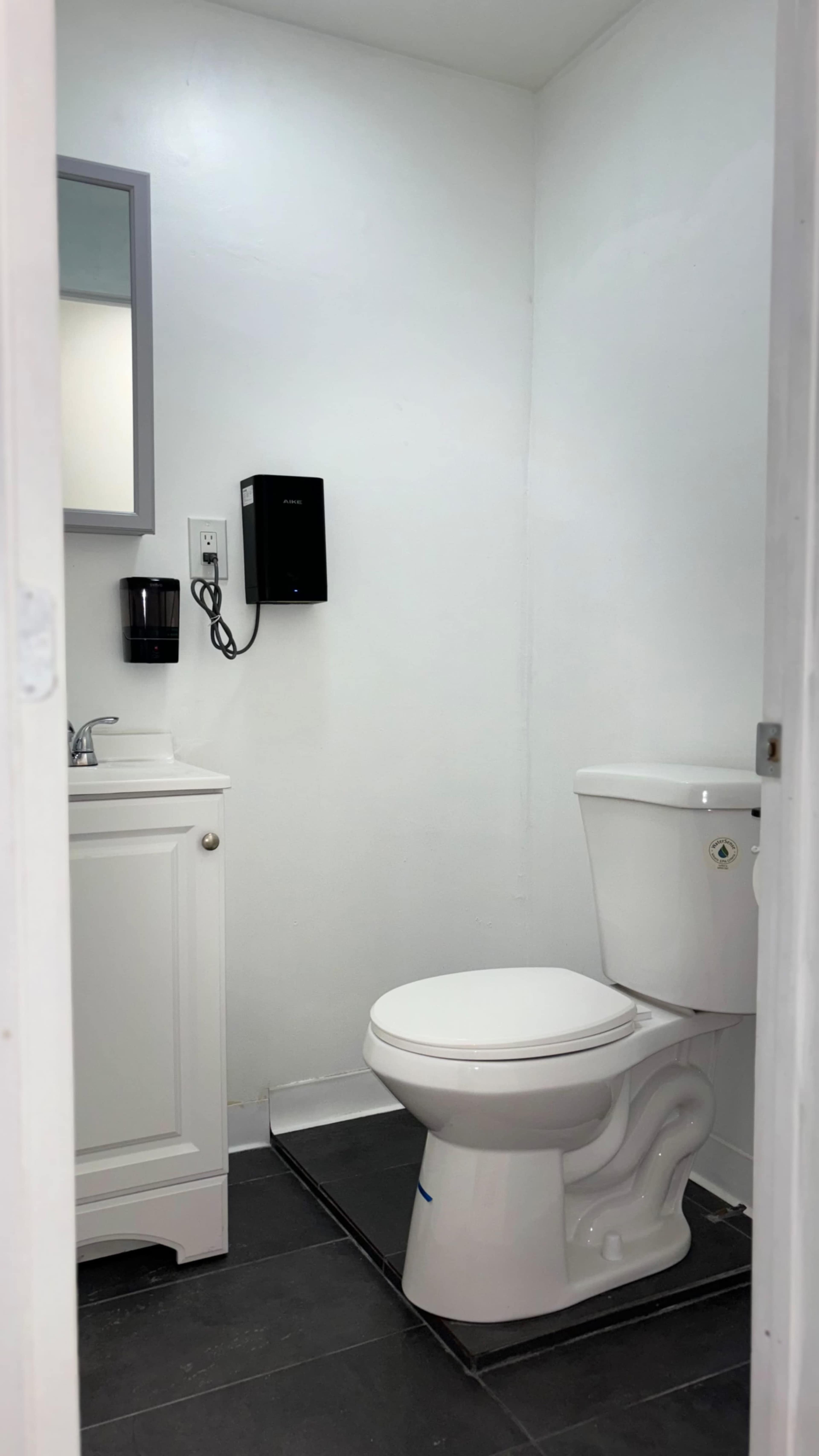 A small, clean restroom featuring a toilet, a sink with a cabinet below, and a hand dryer on the wall.