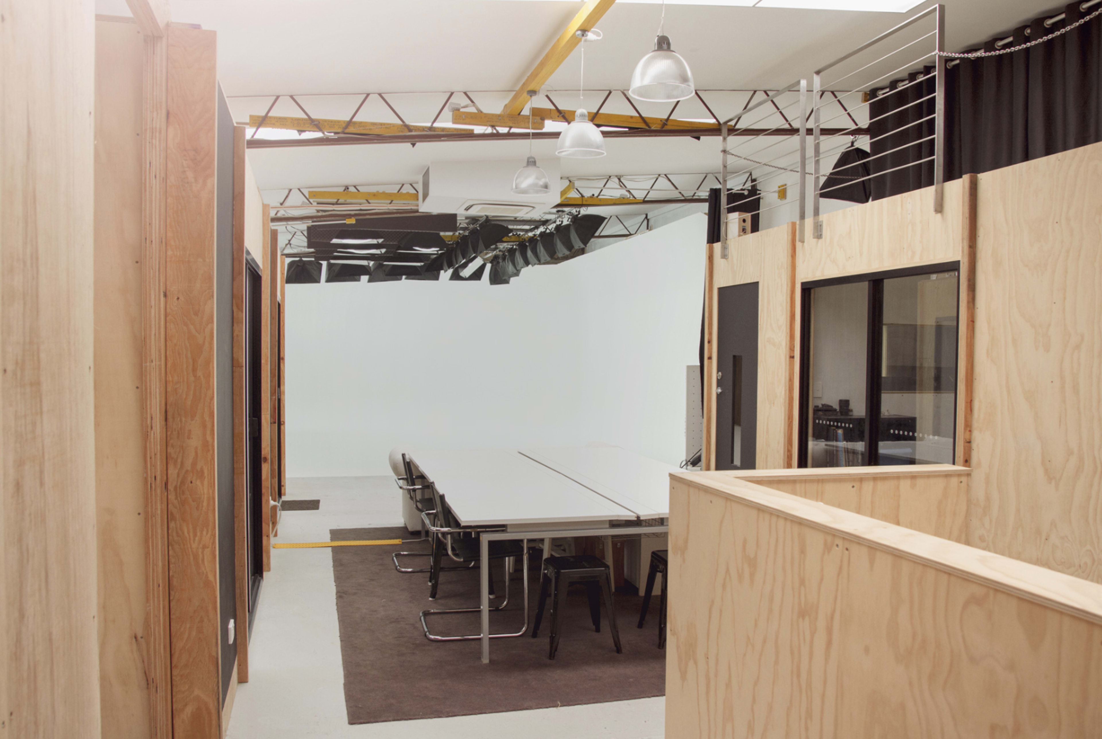 The image shows a modern office space featuring a long conference table surrounded by chairs, with wooden walls and a bright, open area.