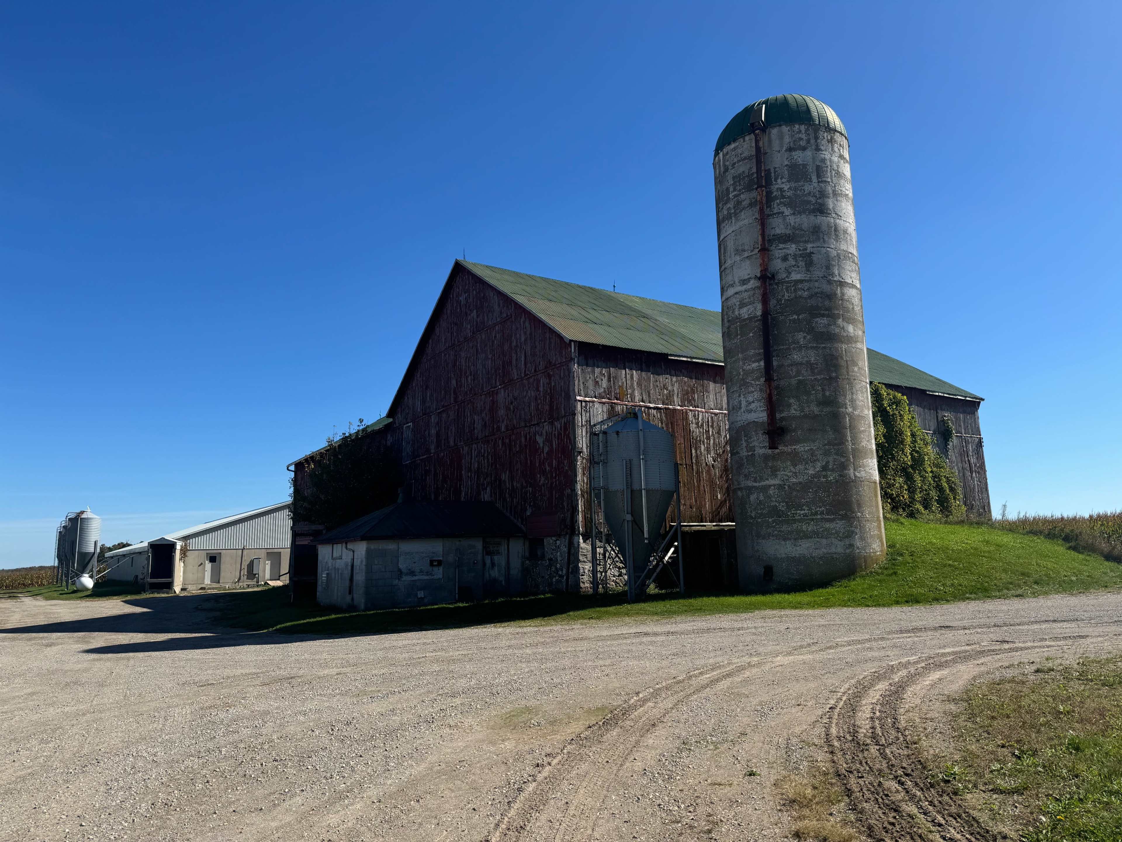 A red barn with a concrete silo stands beside a gravel road under a clear blue sky.