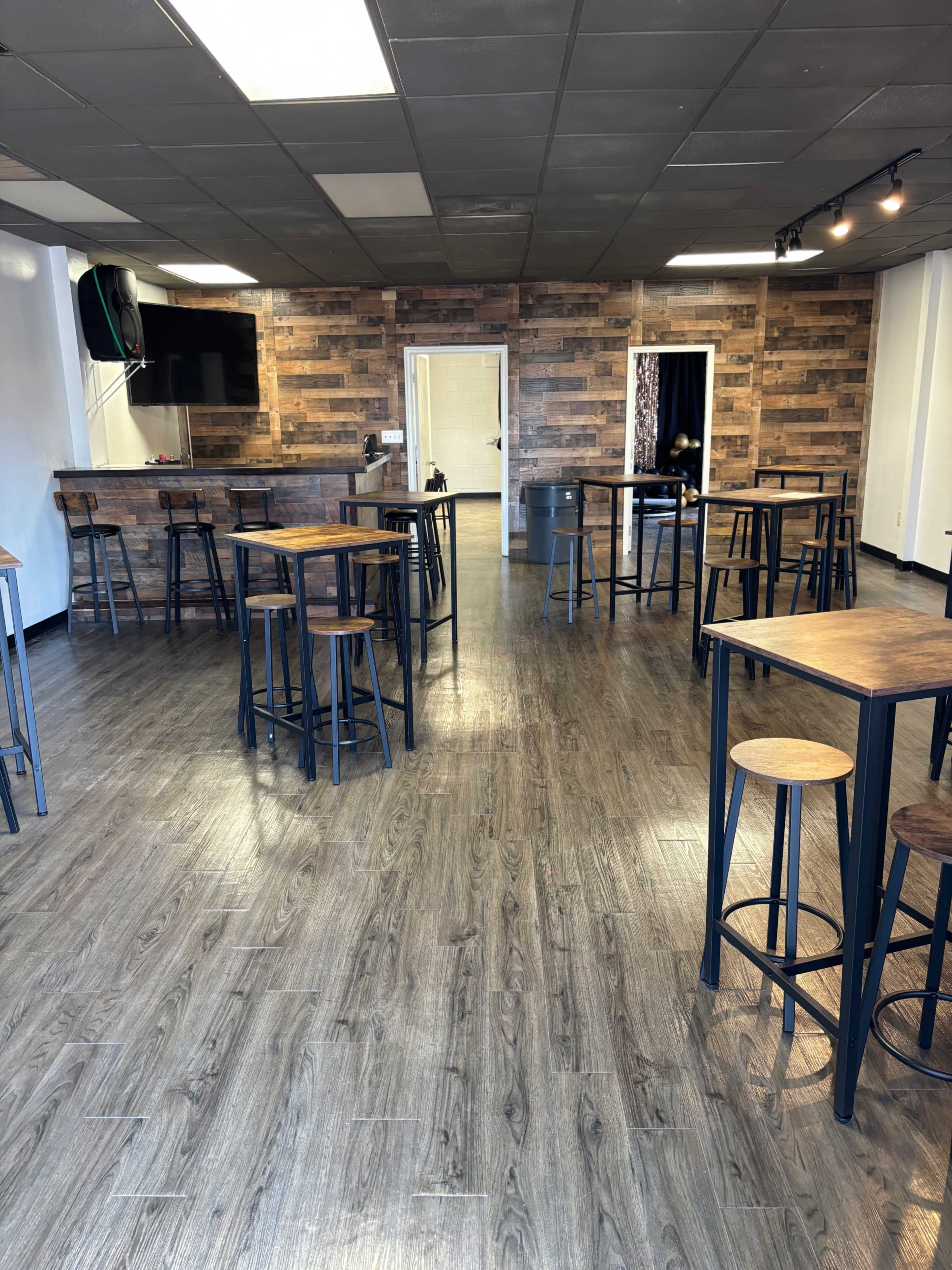 A spacious interior of a café or event space with wooden walls and multiple high tables surrounded by stools.