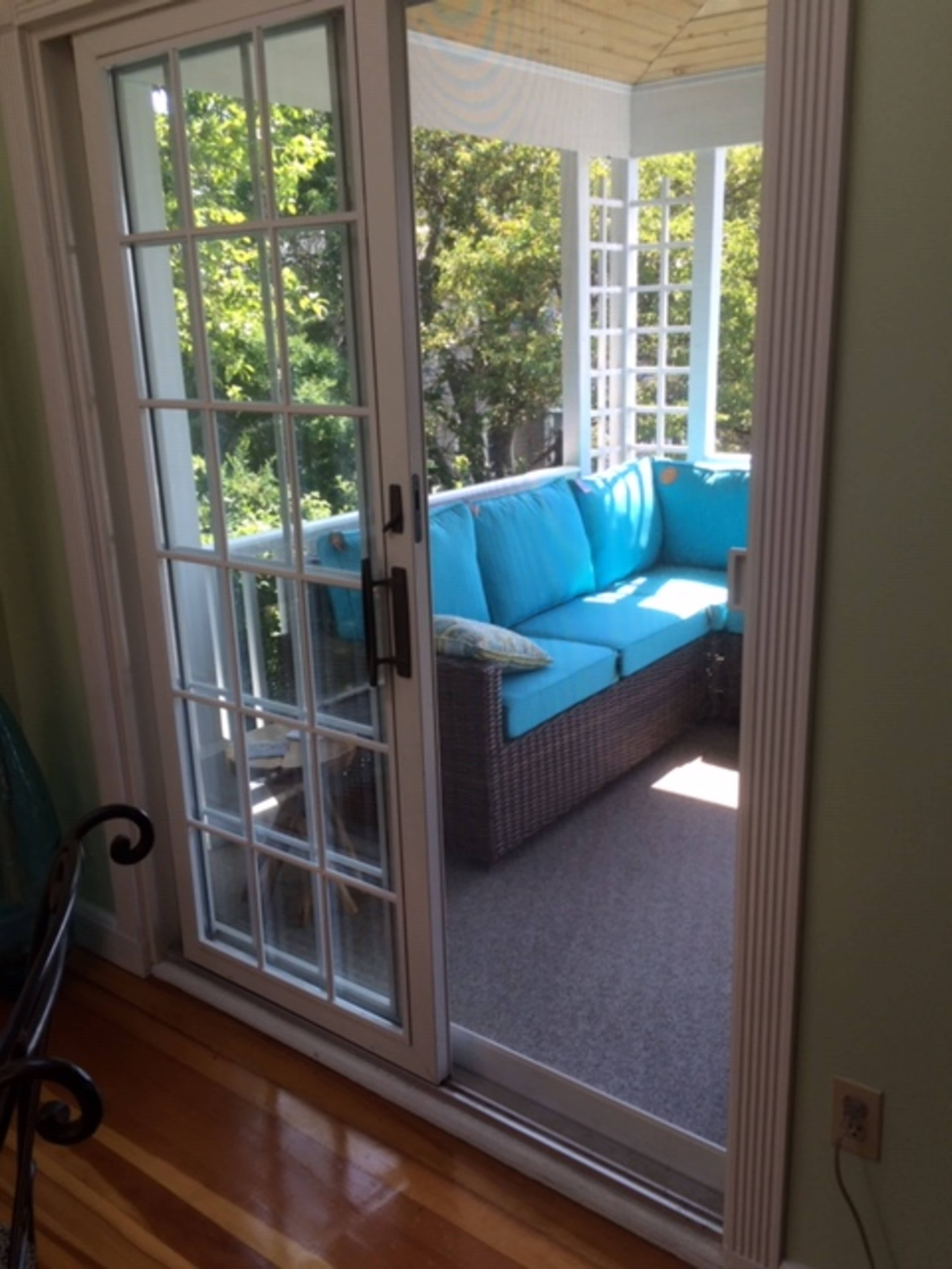 A sliding glass door leads to a sunlit porch with a turquoise couch and wicker furniture.