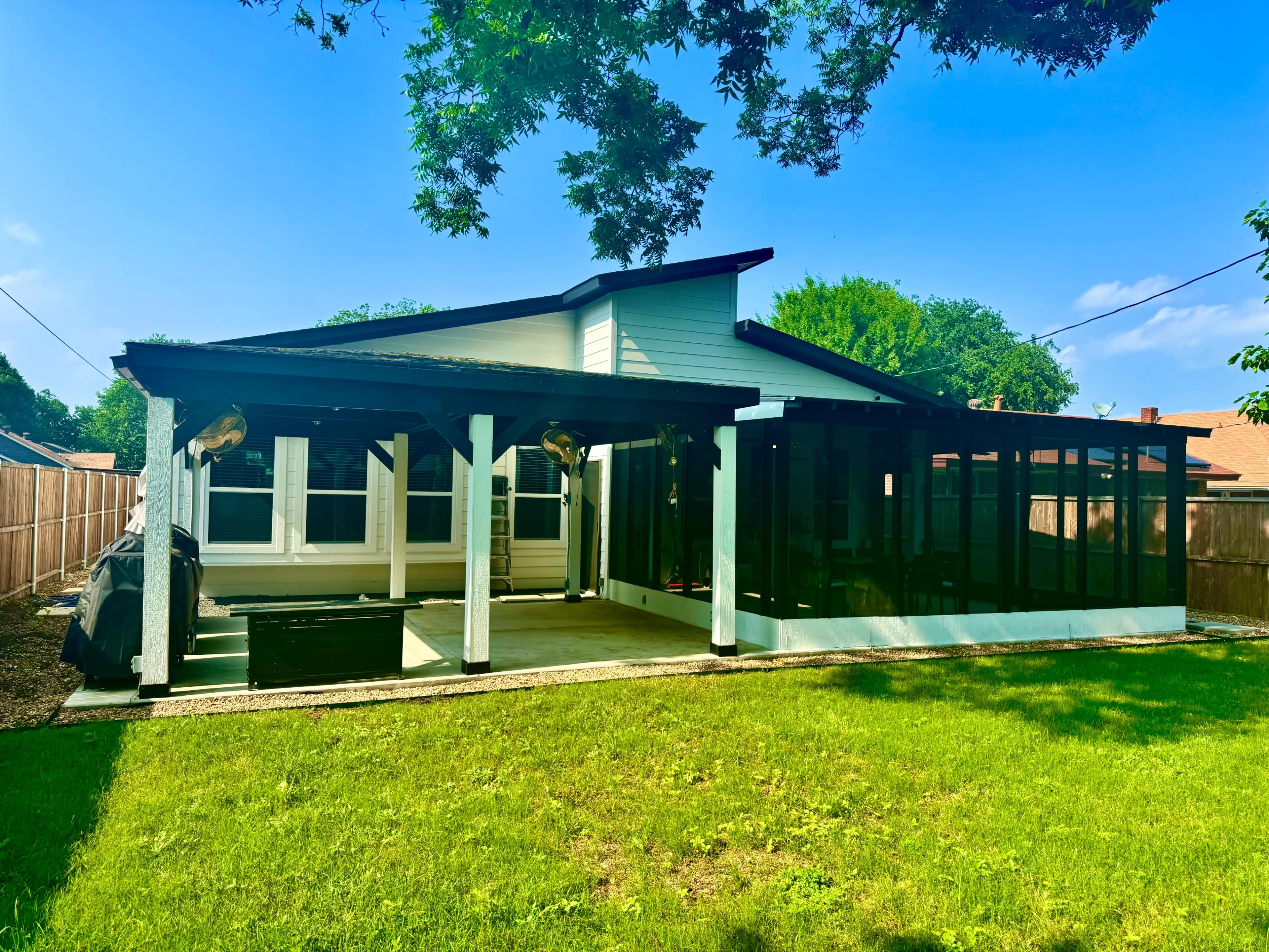 A single-story house with a large screened porch, surrounded by a lawn and trees.
