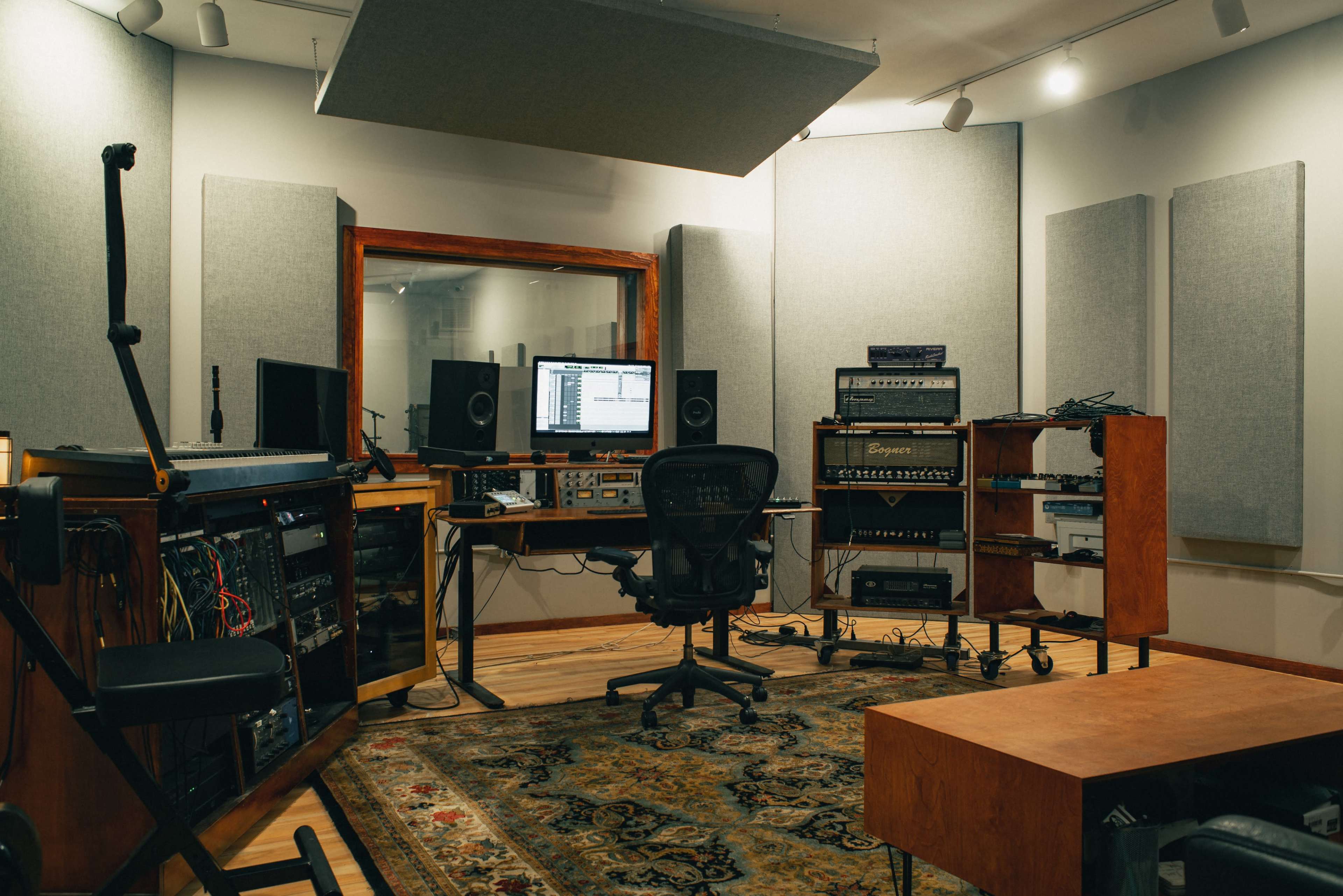 A recording studio features a central workspace with audio equipment, monitors, and soundproof panels on the walls.