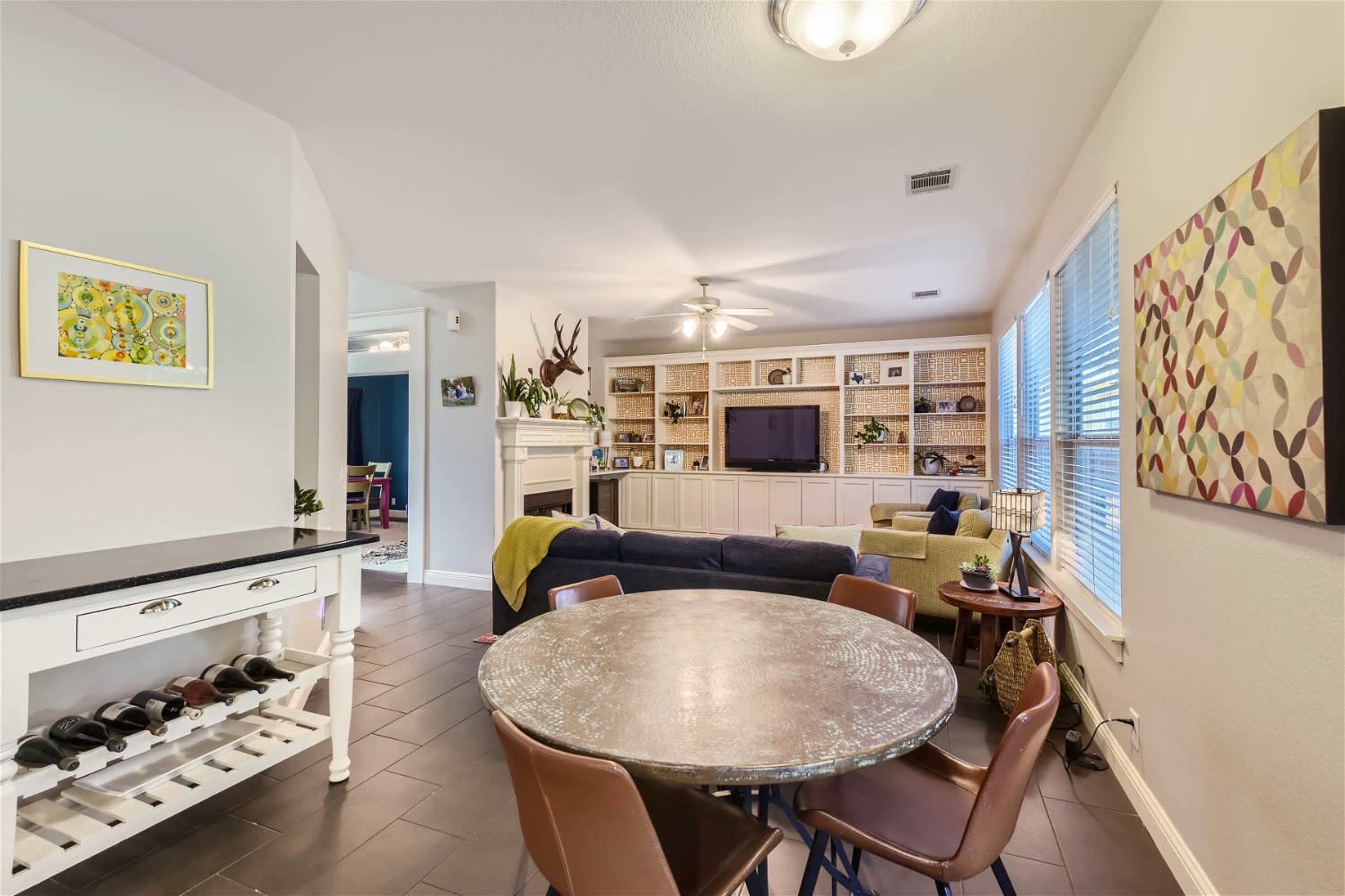 A living space with a circular dining table and chairs, a TV in a built-in shelf unit, and a cozy seating area.