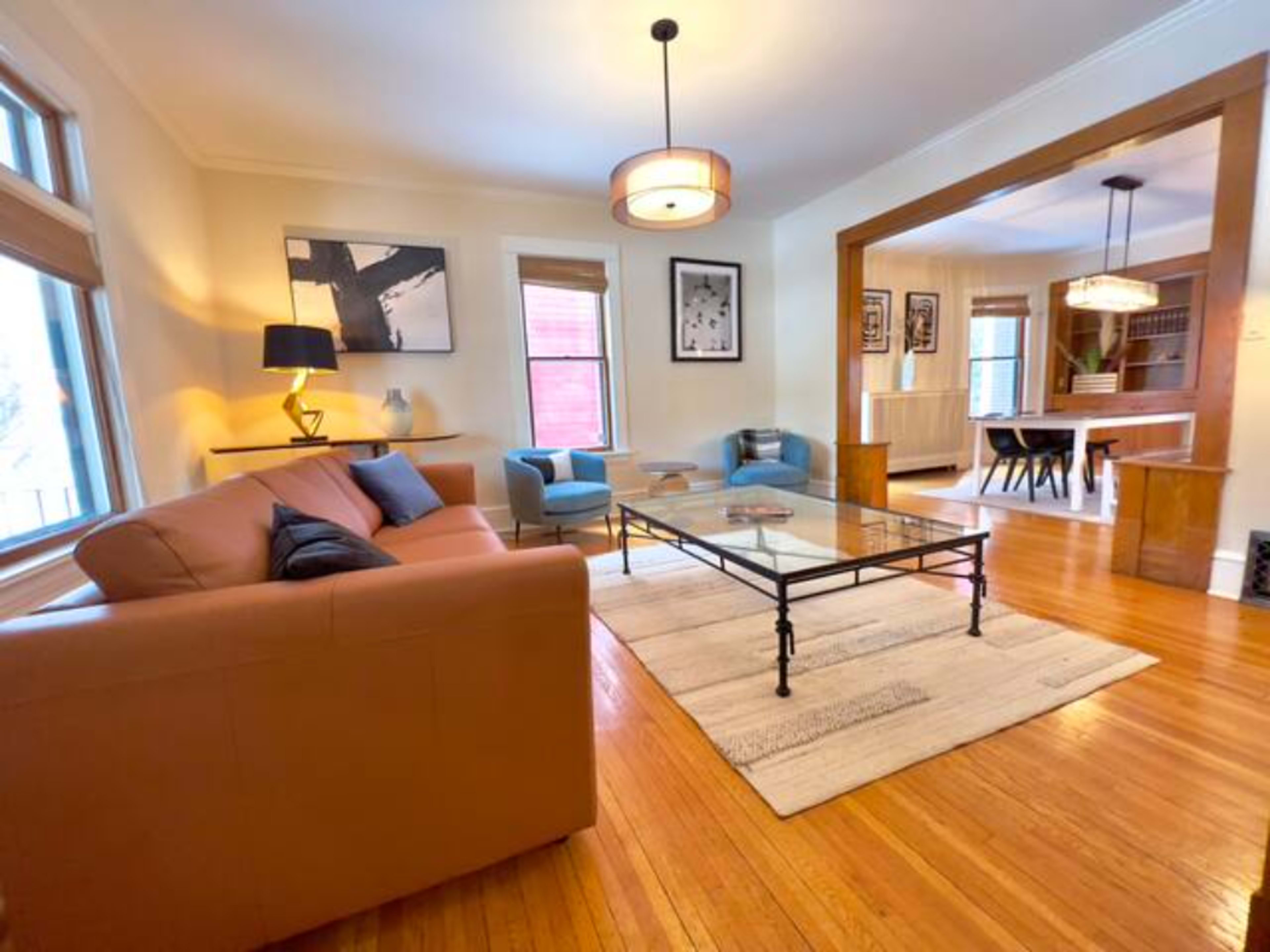 The living room features a brown sofa, a glass coffee table, two blue chairs, and hardwood flooring with a rug.