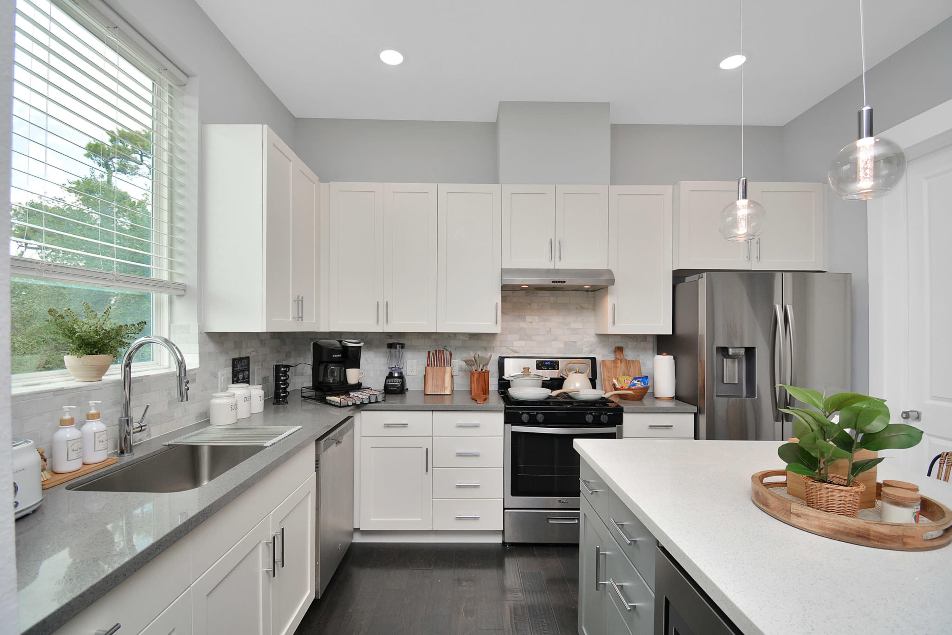 A modern kitchen with white cabinets, stainless steel appliances, and a countertop island featuring a small plant arrangement.