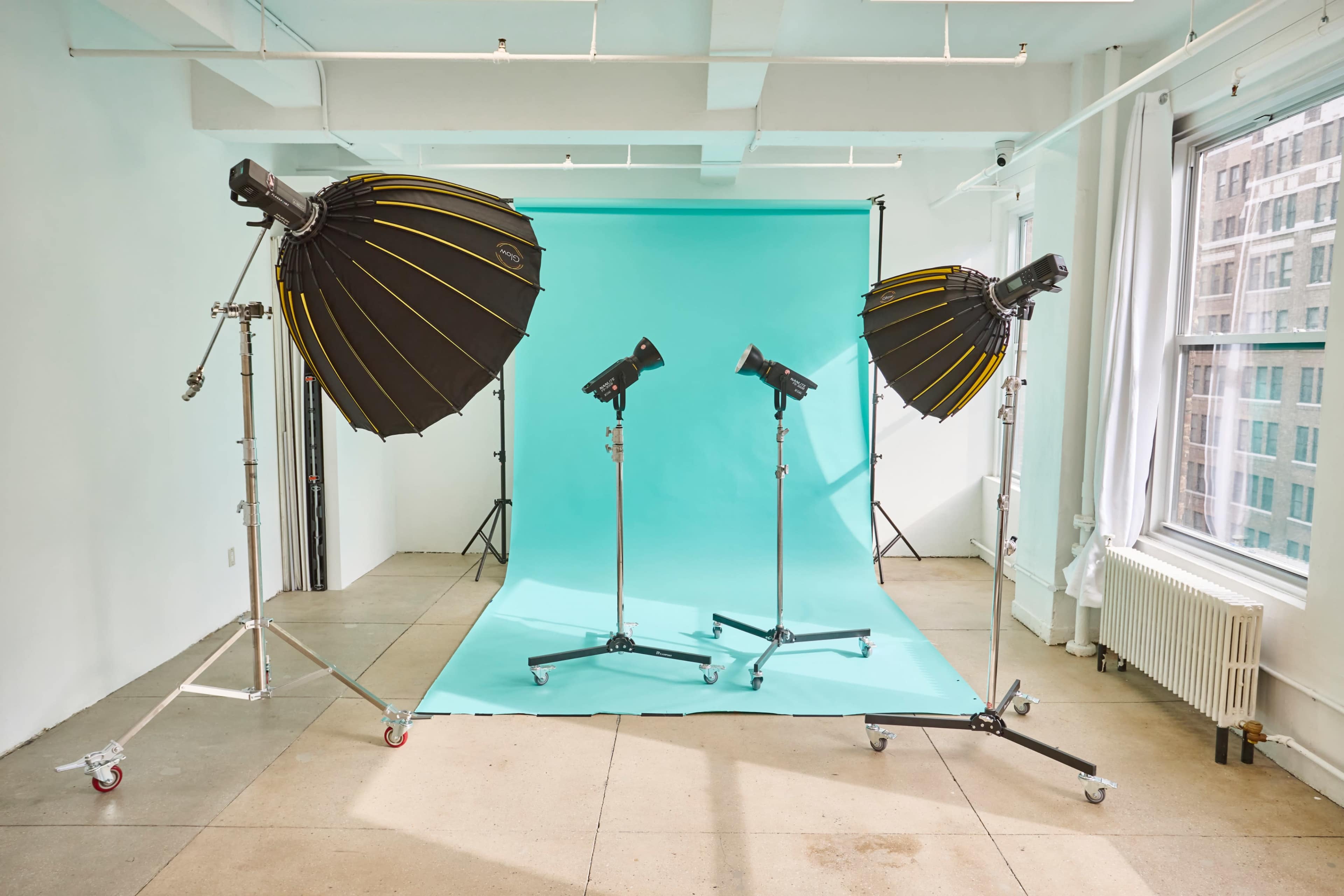 The image shows a photography studio setup with three lighting units and a bright turquoise backdrop.