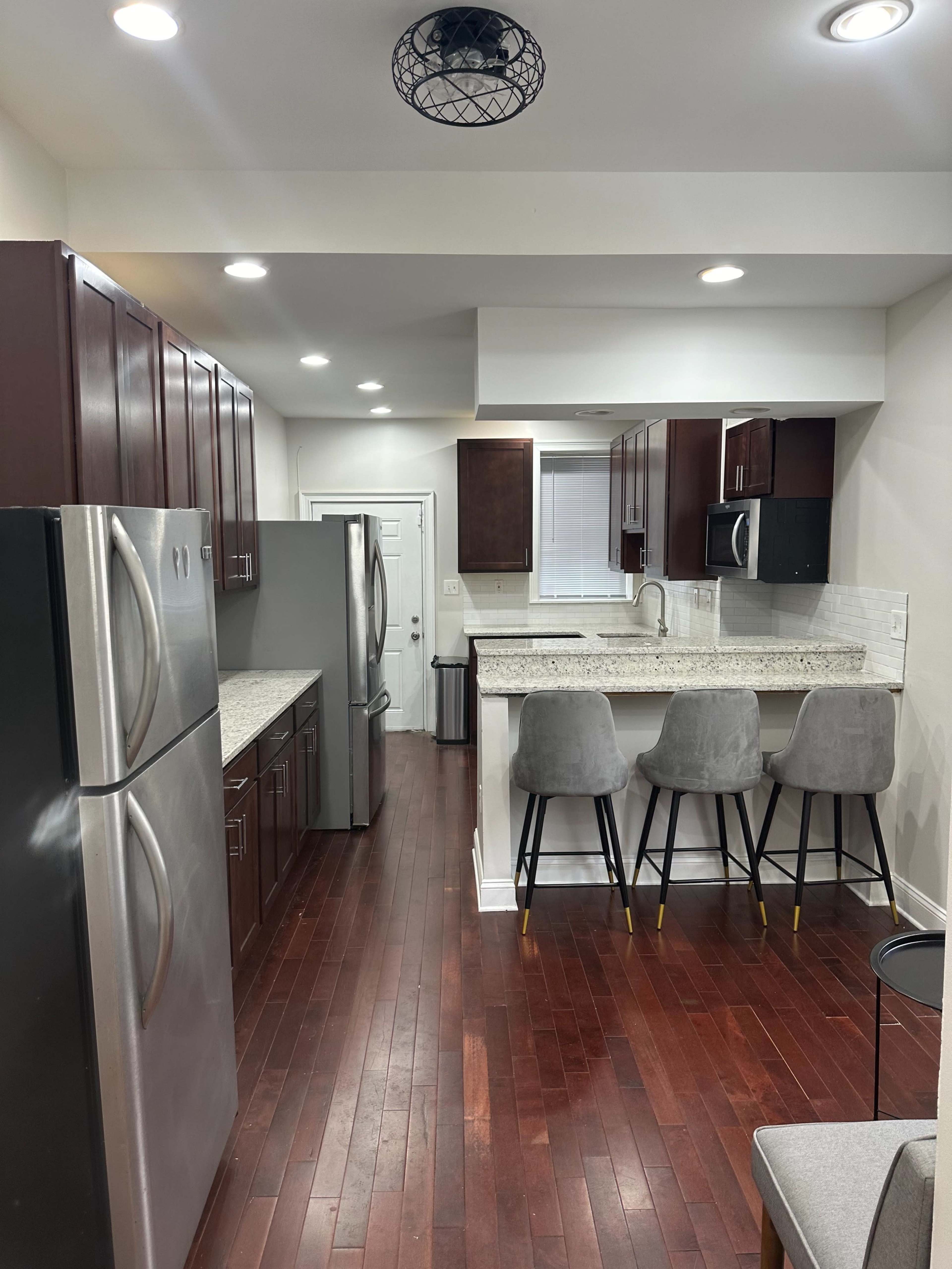 A modern kitchen featuring dark wood cabinets, stainless steel appliances, a granite countertop, and three gray barstools at a kitchen island.