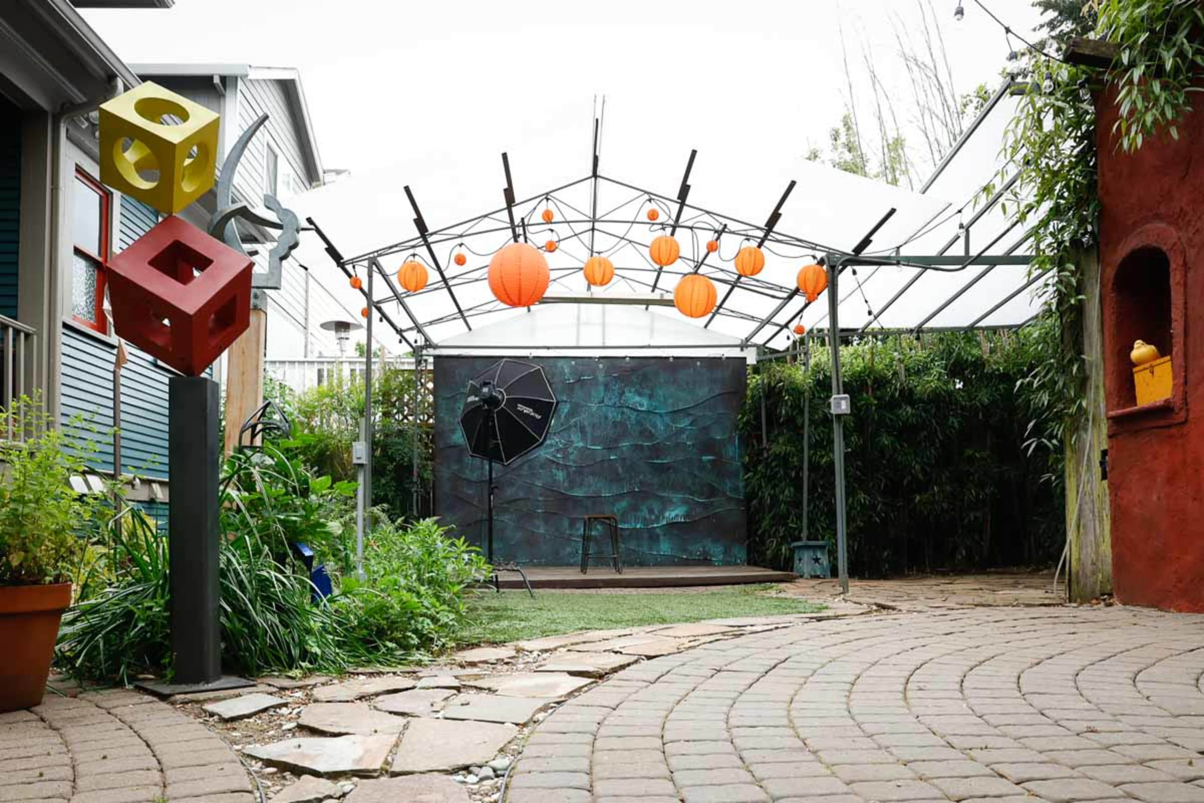 An outdoor photography studio with a transparent canopy, colorful hanging lanterns, and a backdrop against a landscaped garden.