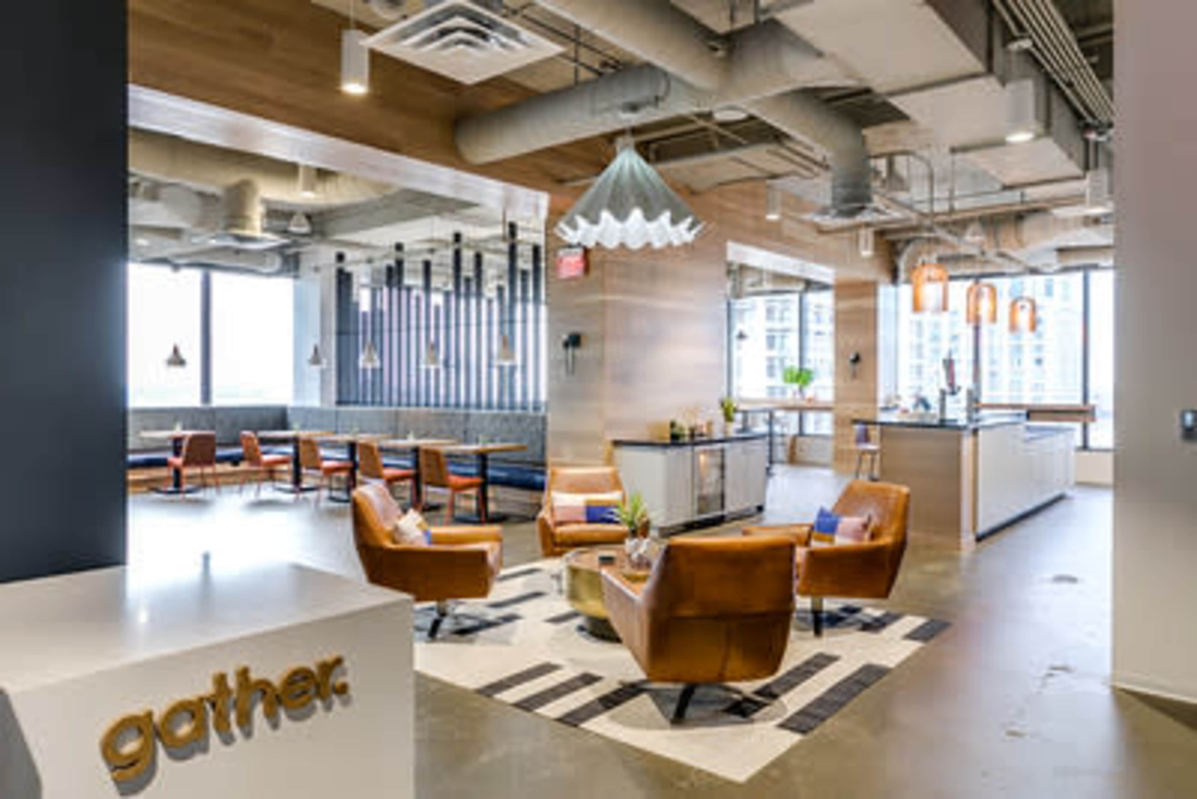 The image shows a modern, open office space featuring brown leather chairs, a reception desk with the word "gather," and large windows providing natural light.