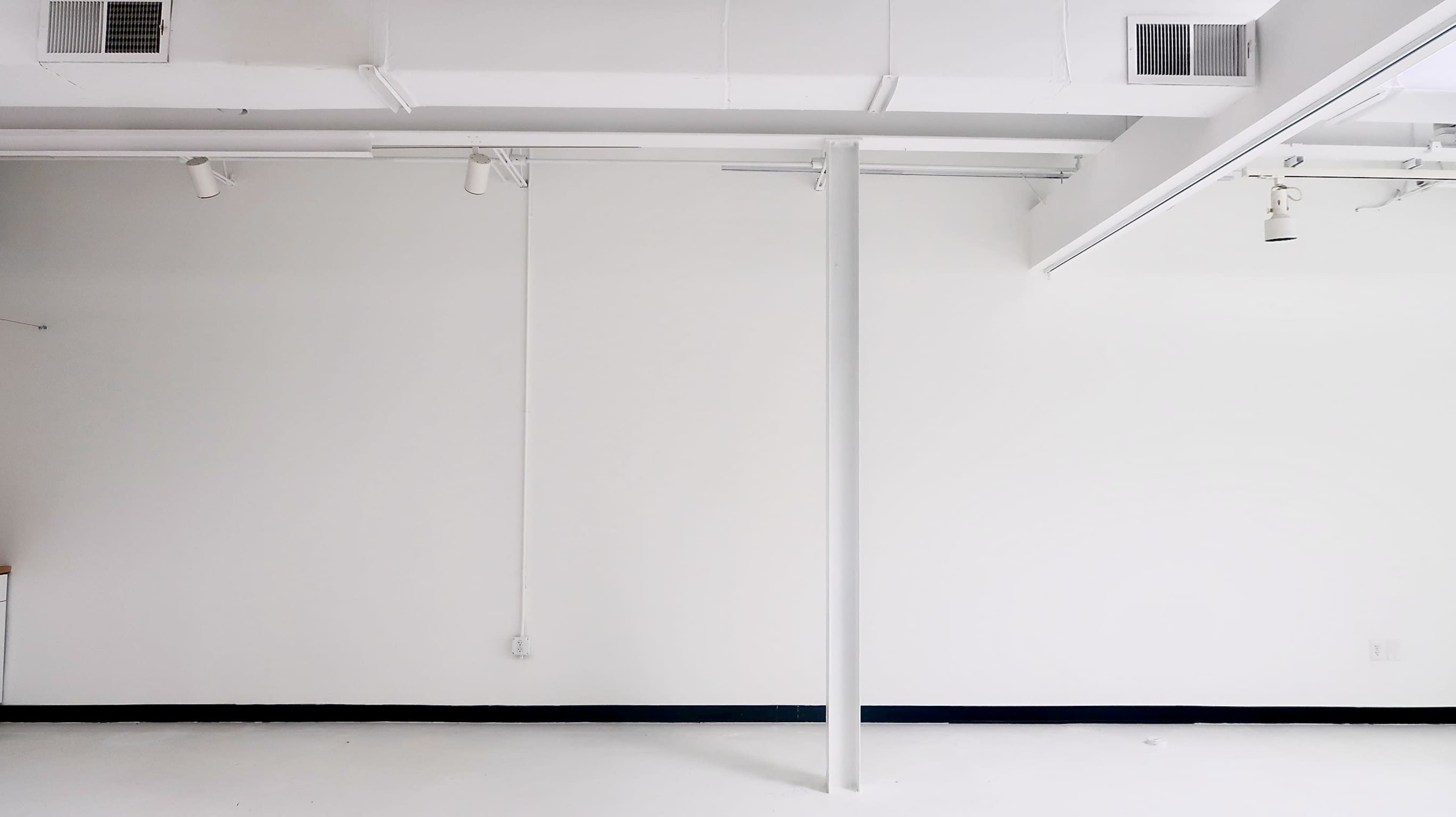 The image shows a minimalistic, empty room with white walls, a white ceiling, and a central support column.