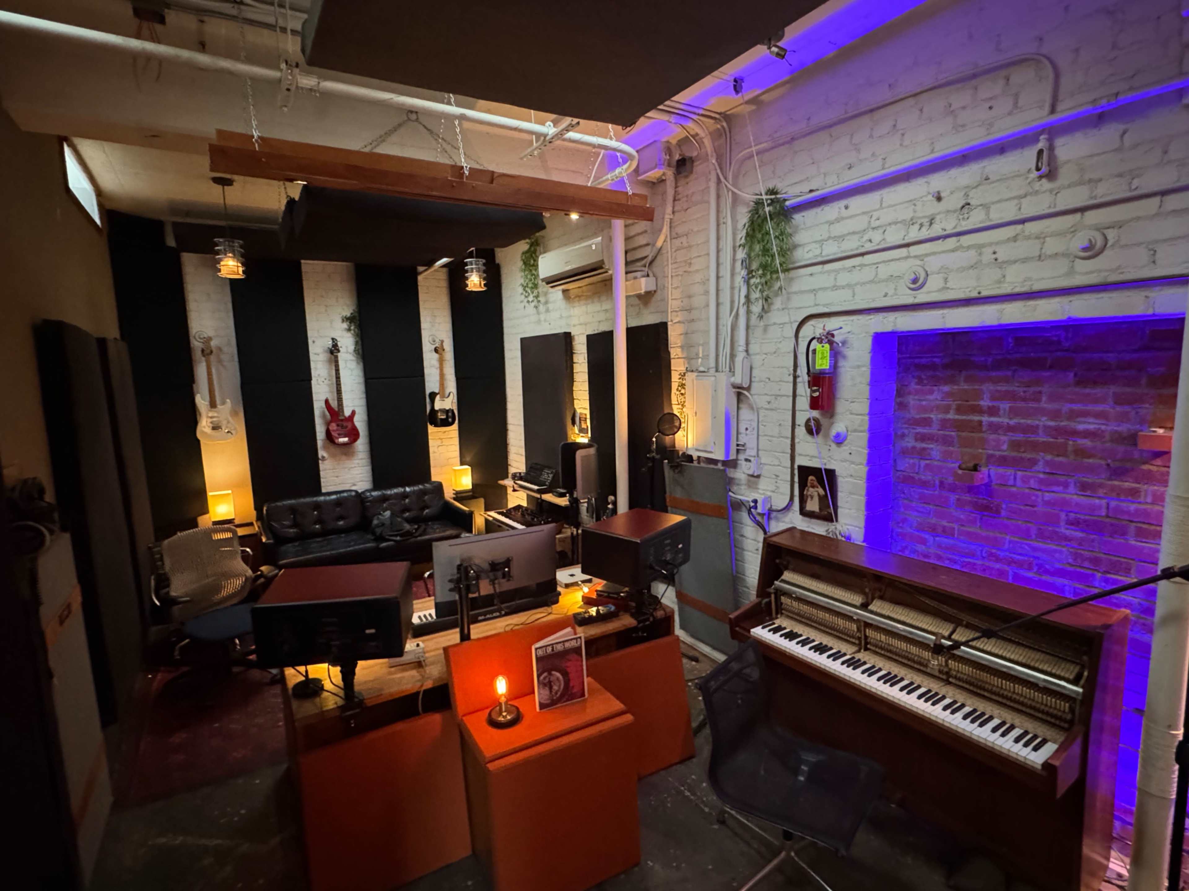The image shows a recording studio with various musical instruments, a piano, and comfortable seating arranged around a central workspace.