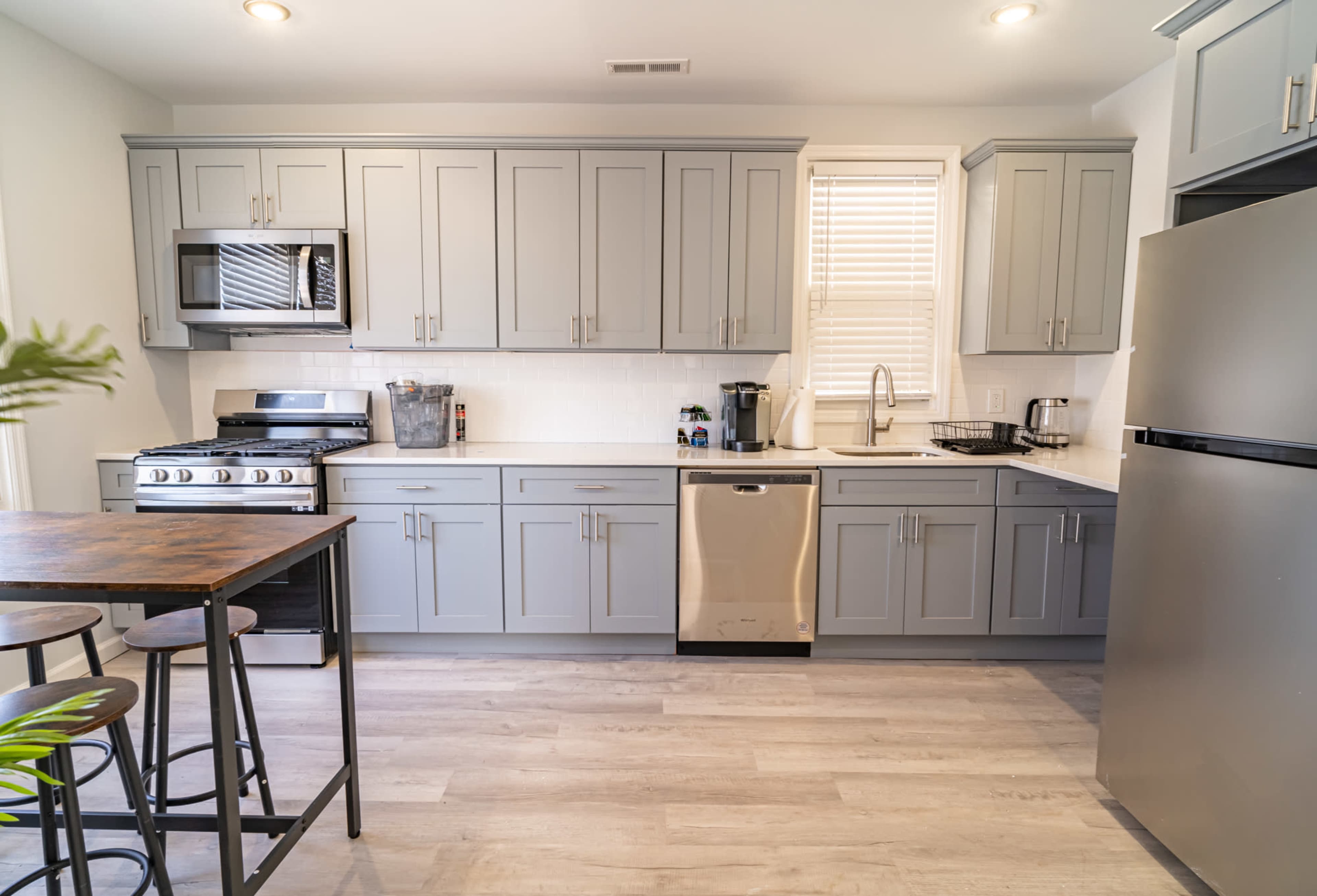 A modern kitchen with gray cabinets, stainless steel appliances, and a wooden dining table with metal stools.