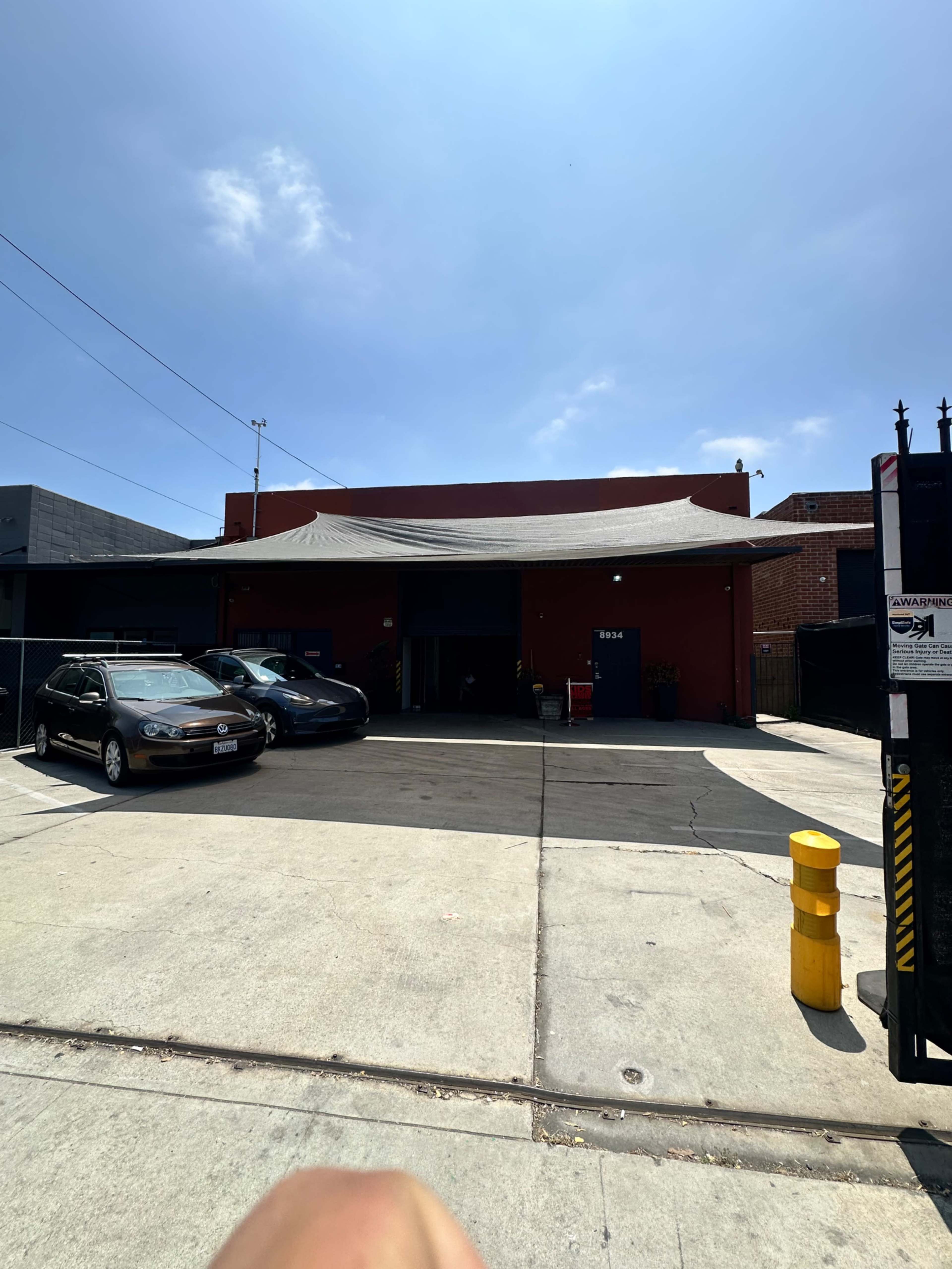 A red brick building with a large canopy is visible, situated in a parking lot alongside several cars and a yellow parking post.