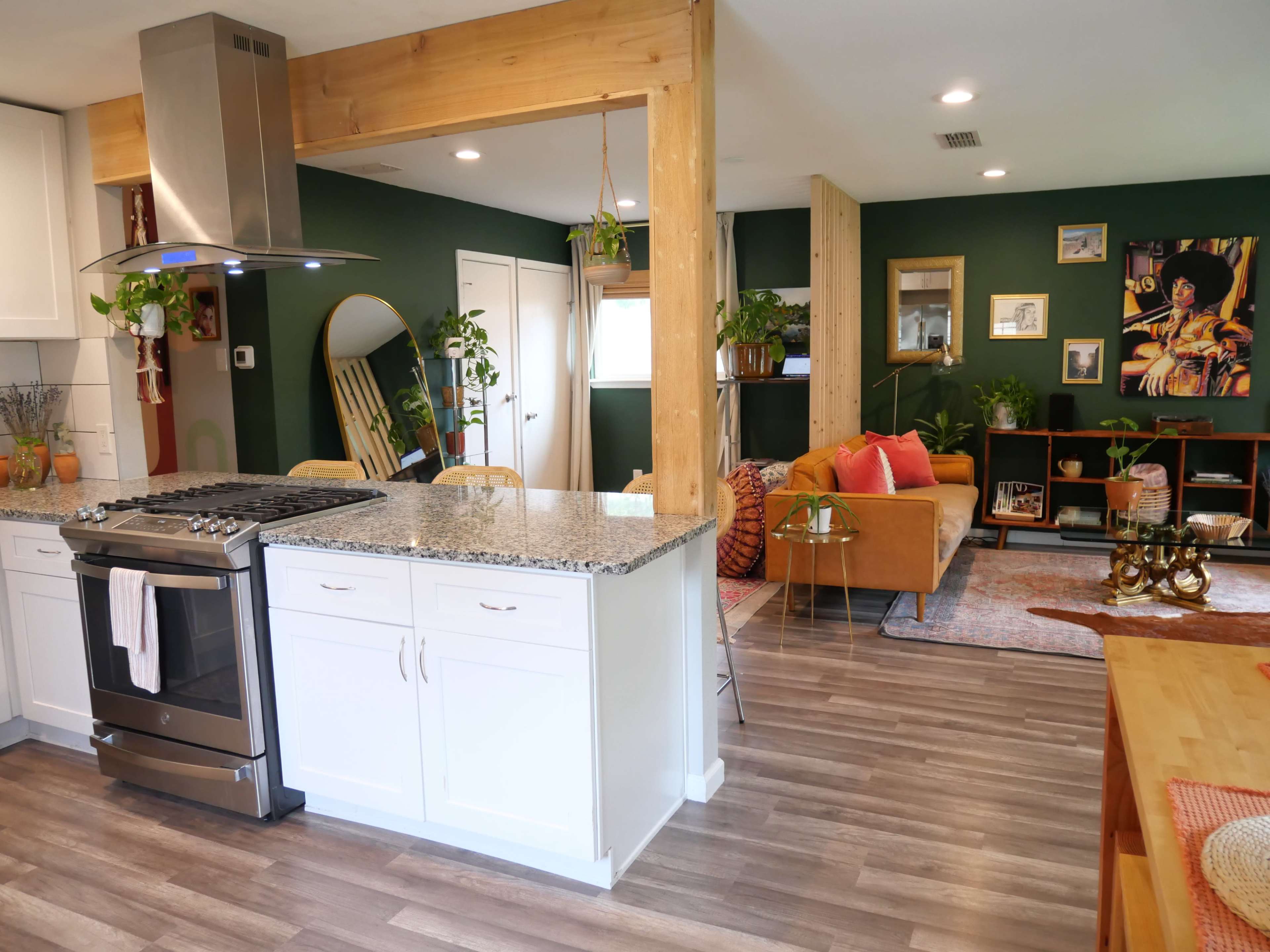 A modern kitchen and living room area with green walls, granite countertops, and wooden accents, featuring a sofa and dining space.