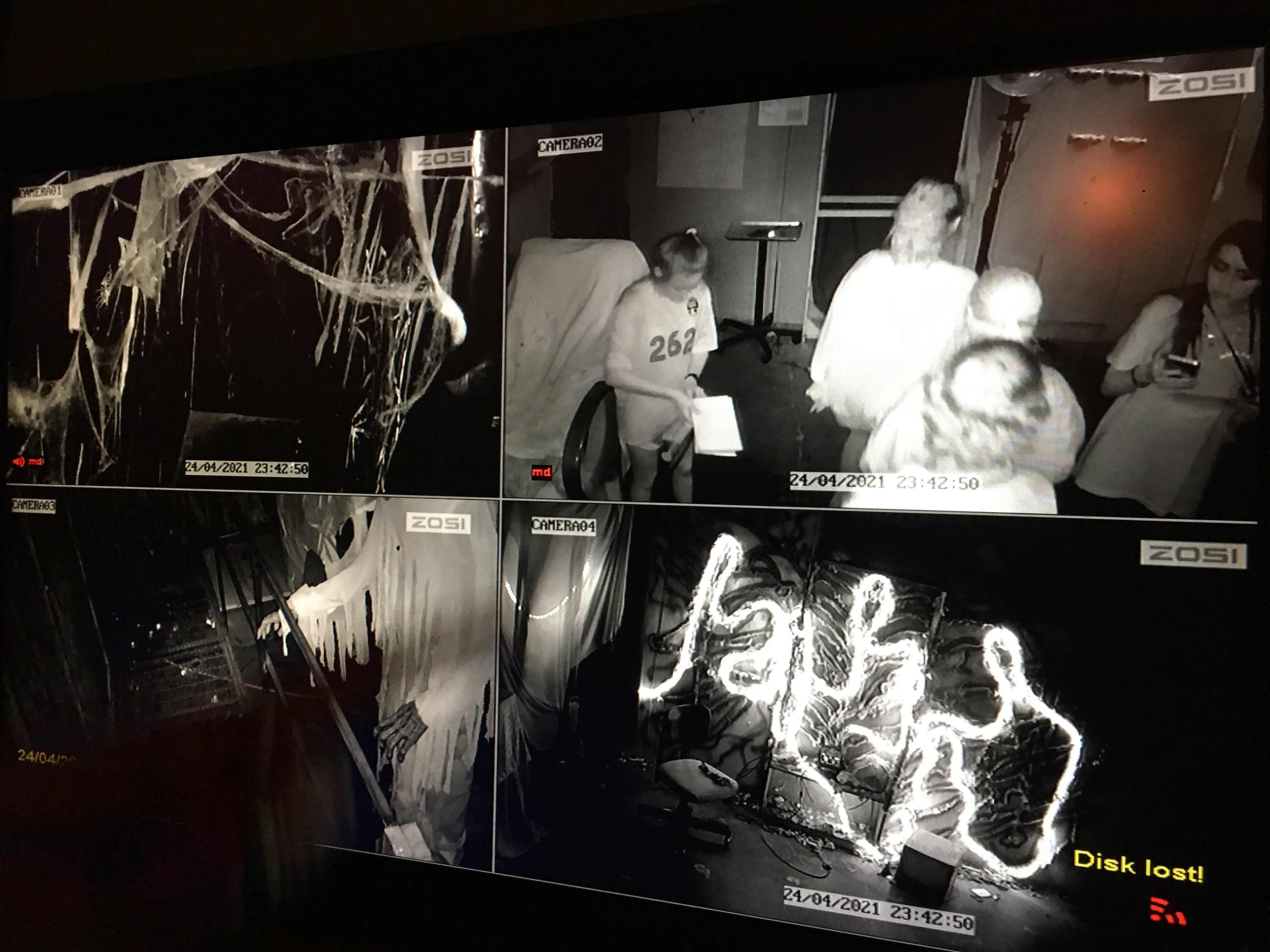 Multiple surveillance camera feeds, featuring dimly lit rooms decorated with cobwebs and ghostly figures, along with a warning message about a lost disk.