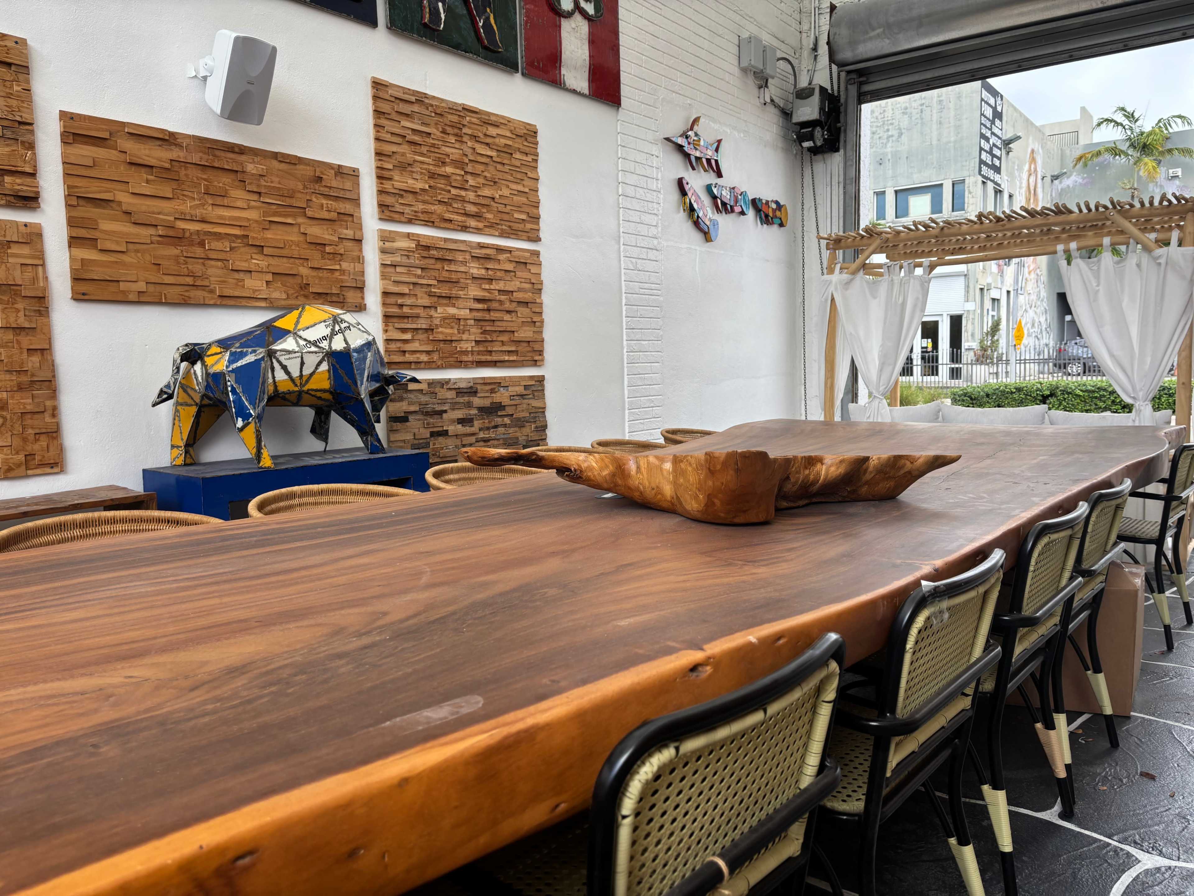 A long wooden table with metal chairs is set in a room adorned with wooden wall panels and a colorful decorative sculpture of a bull.