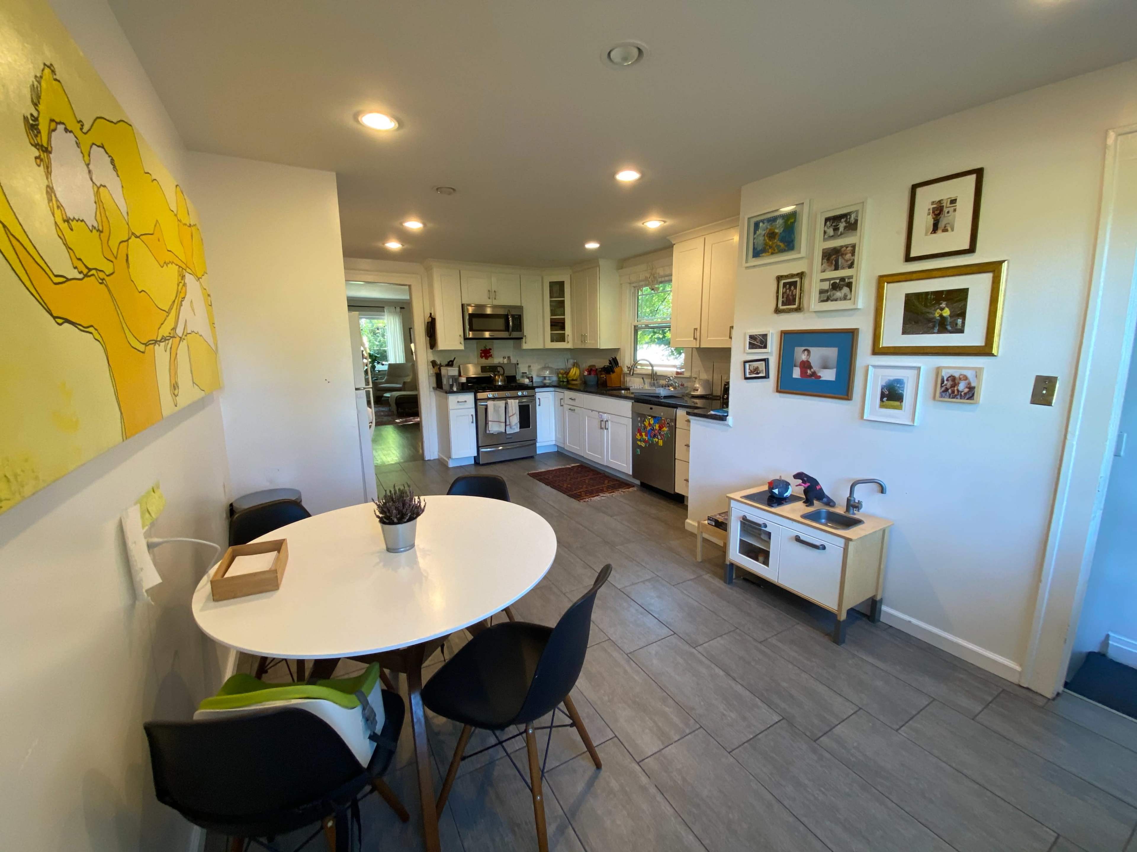 A modern kitchen and dining area featuring a round table with black chairs, white cabinetry, and framed photos on the walls.