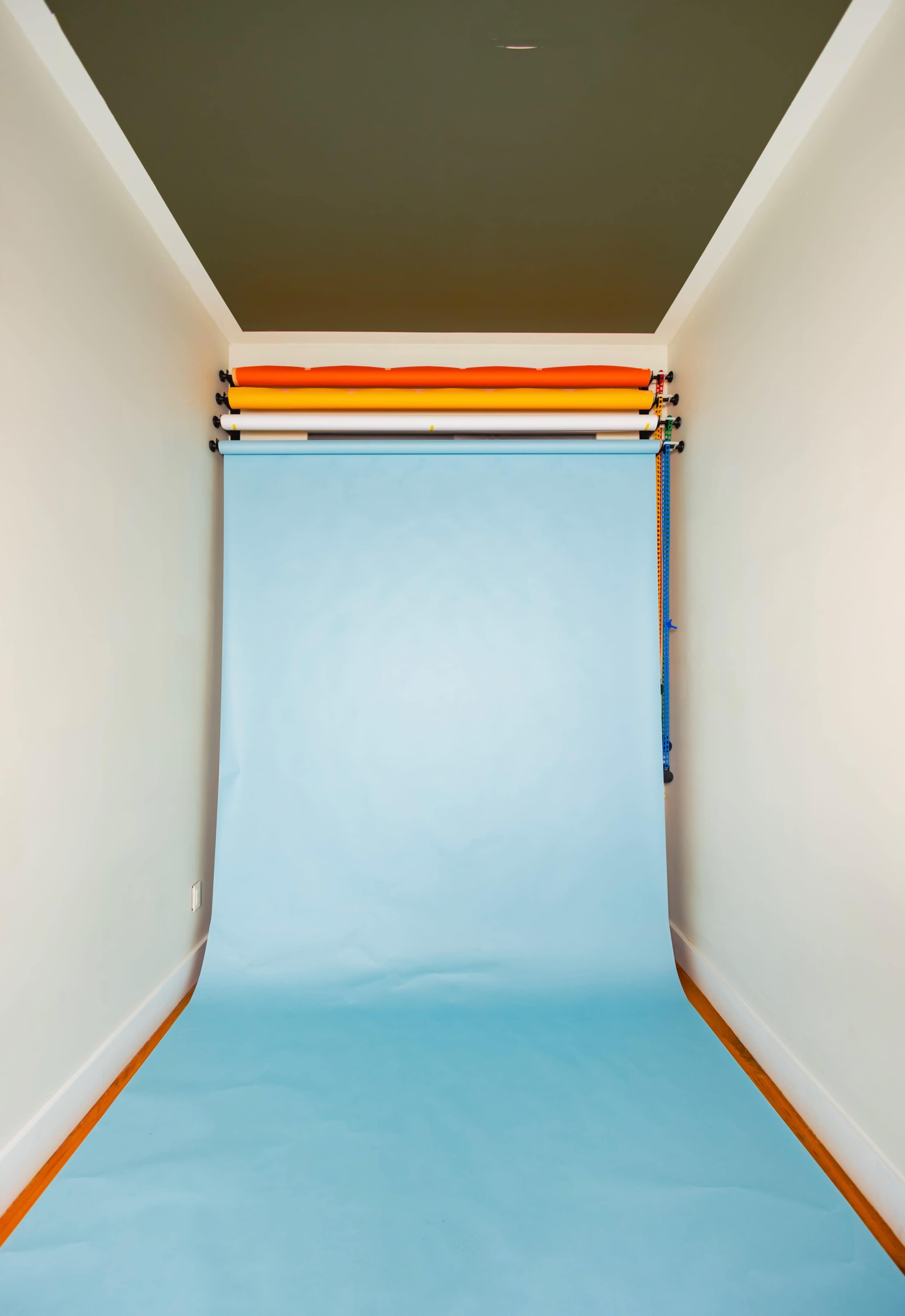 A photo studio setup with a light blue backdrop and colorful paper rolls hanging from the wall.