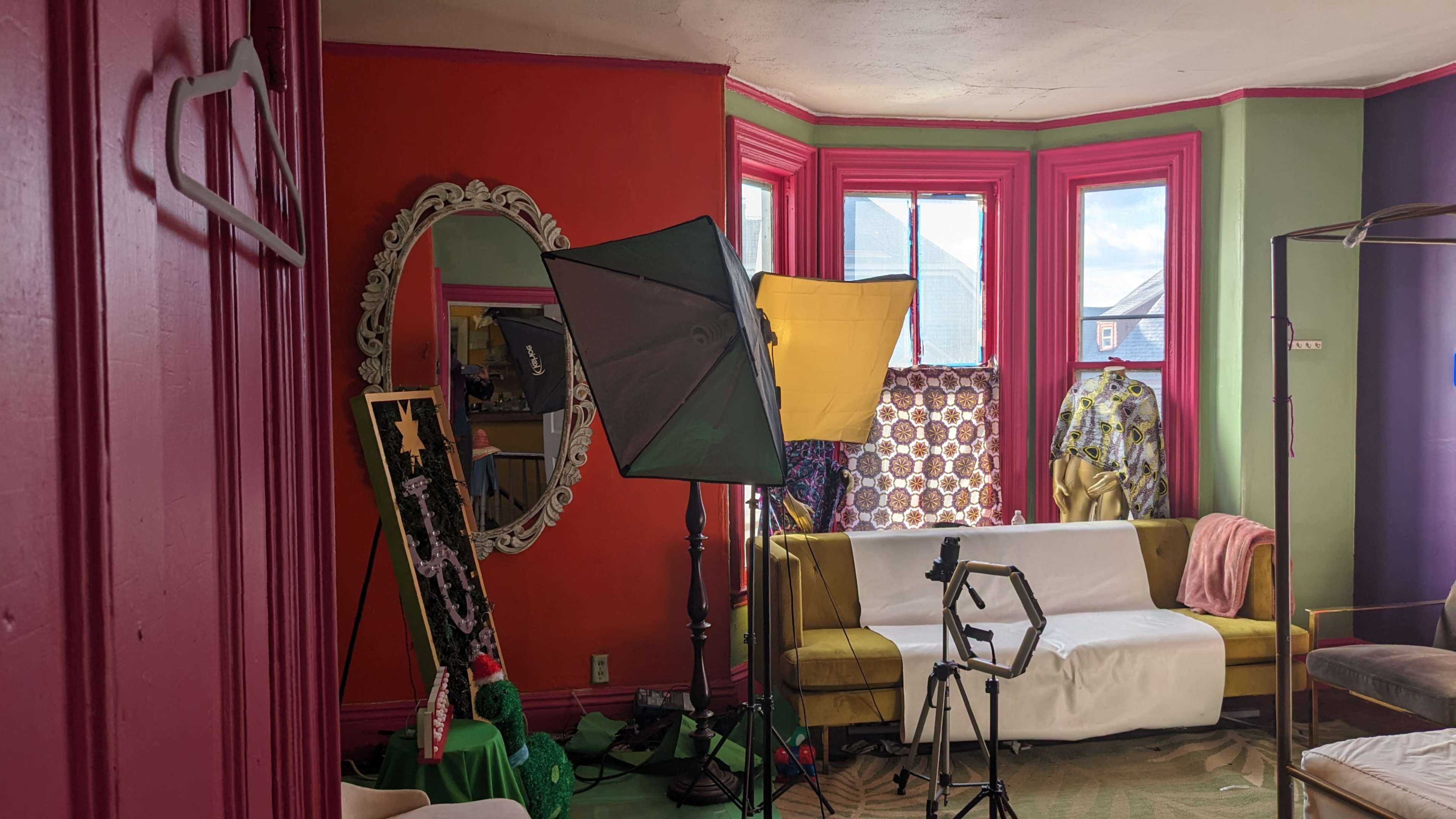 A brightly painted room with a large mirror, a sofa covered in white fabric, and various photography equipment set up for a shoot.