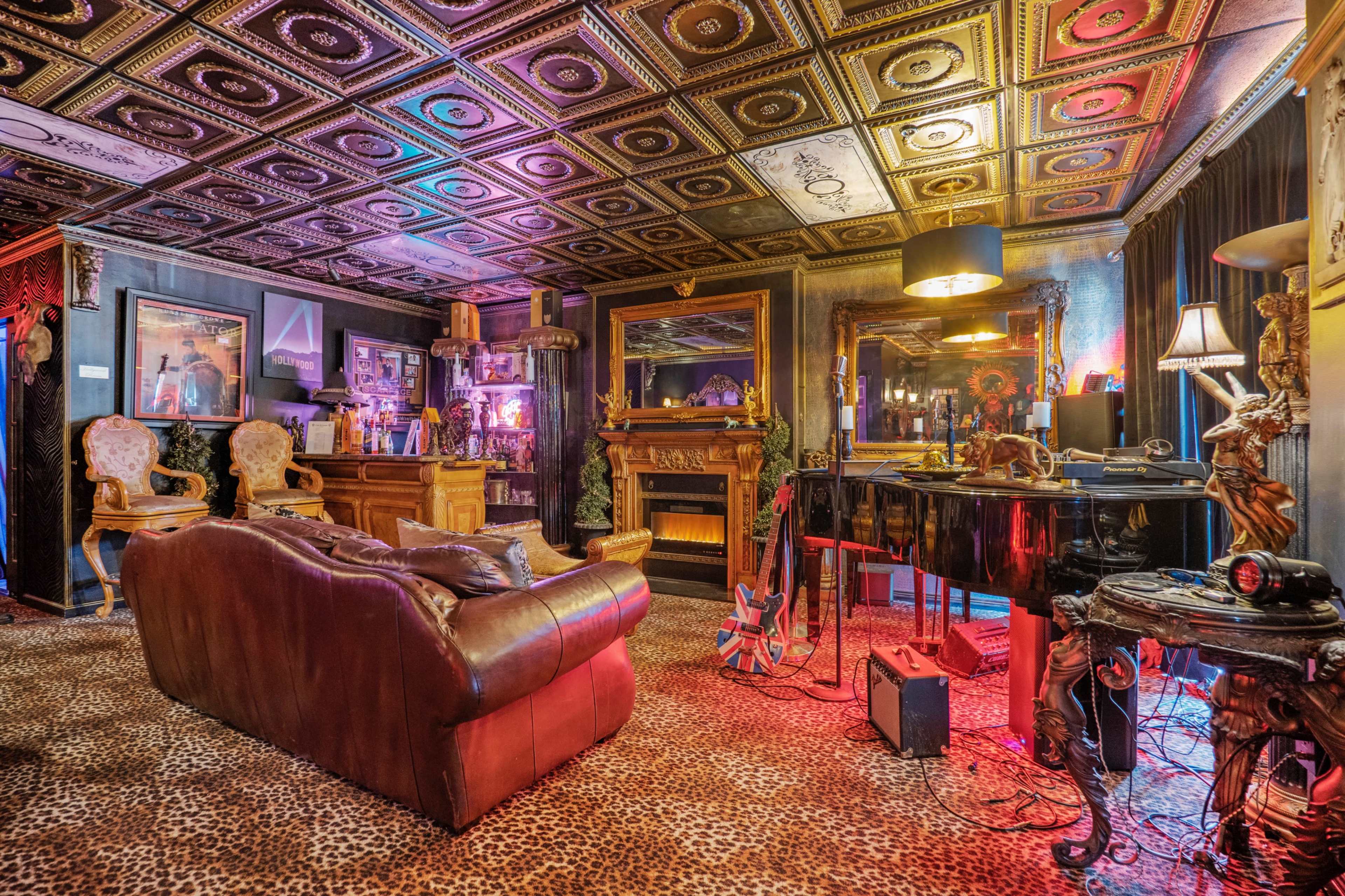 The room features a plush leather sofa, a grand piano, ornate furnishings, and a ceiling adorned with decorative tiles, all set against a backdrop of vibrant lighting and animal print carpet.