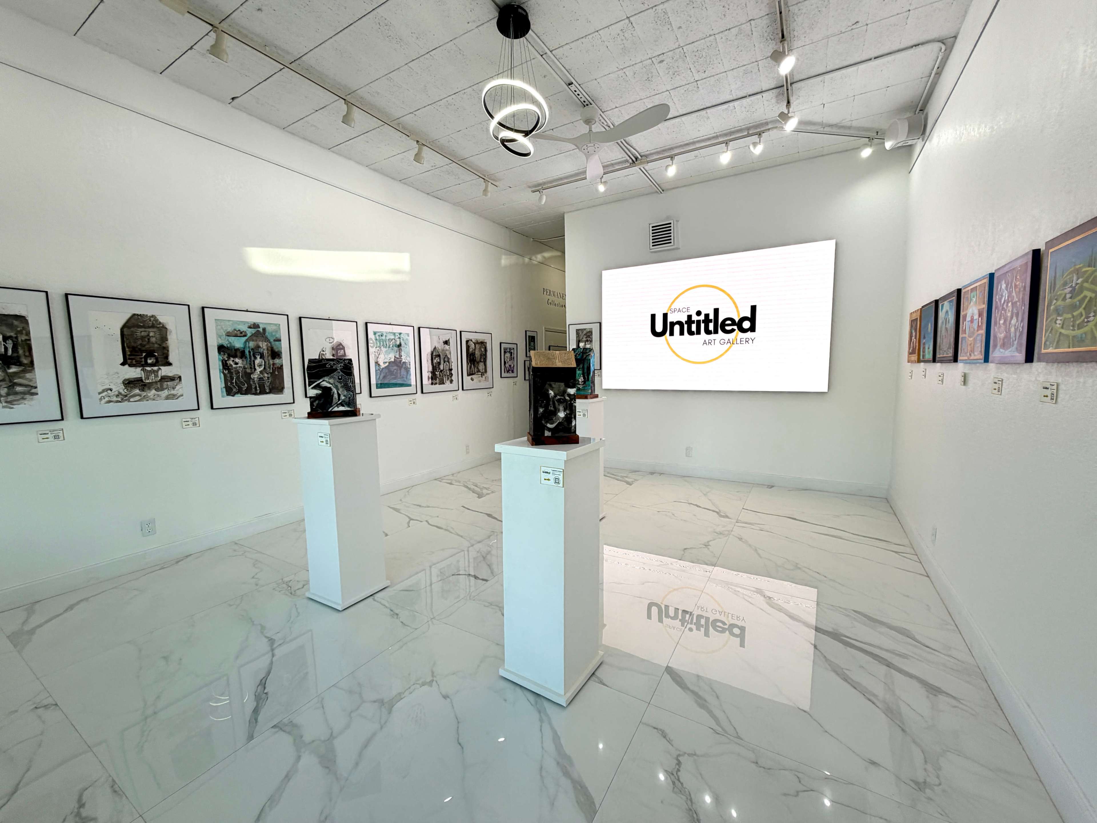 The image shows a modern art gallery featuring white walls, marble flooring, and several framed artworks displayed alongside white pedestals holding sculptures, with a large screen displaying the word "Untitled."