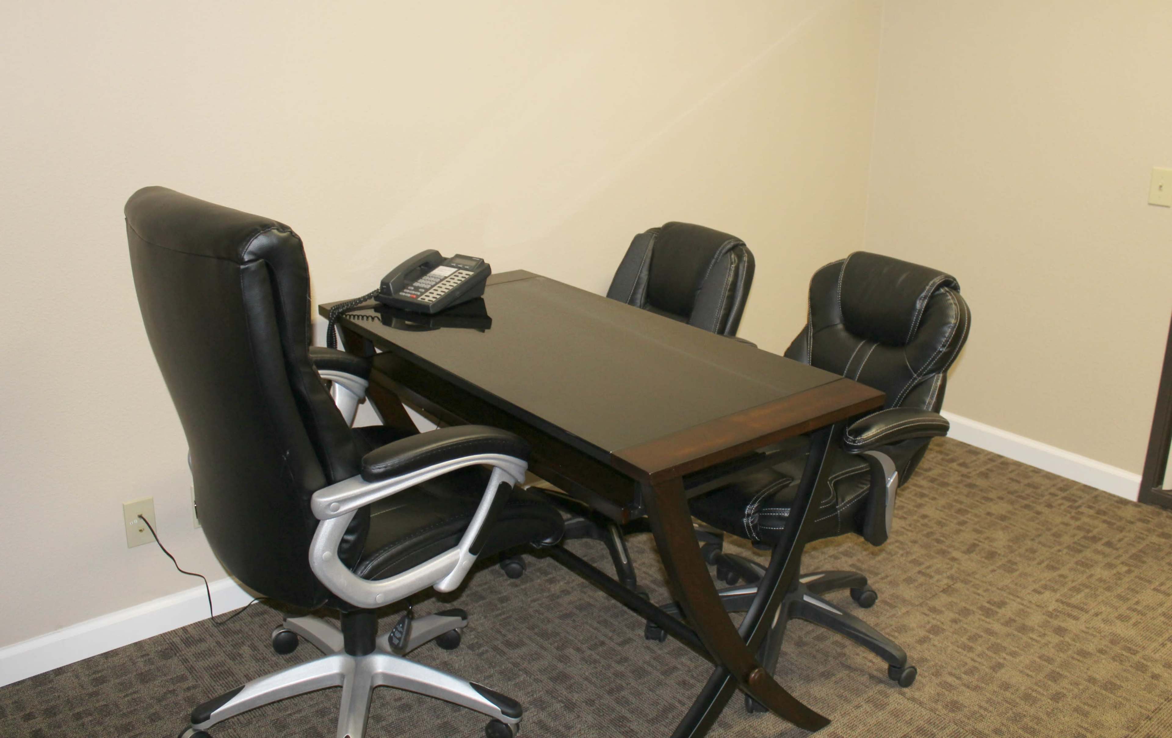 A small office space with a dark wooden table and three black rolling chairs, accompanied by a telephone.