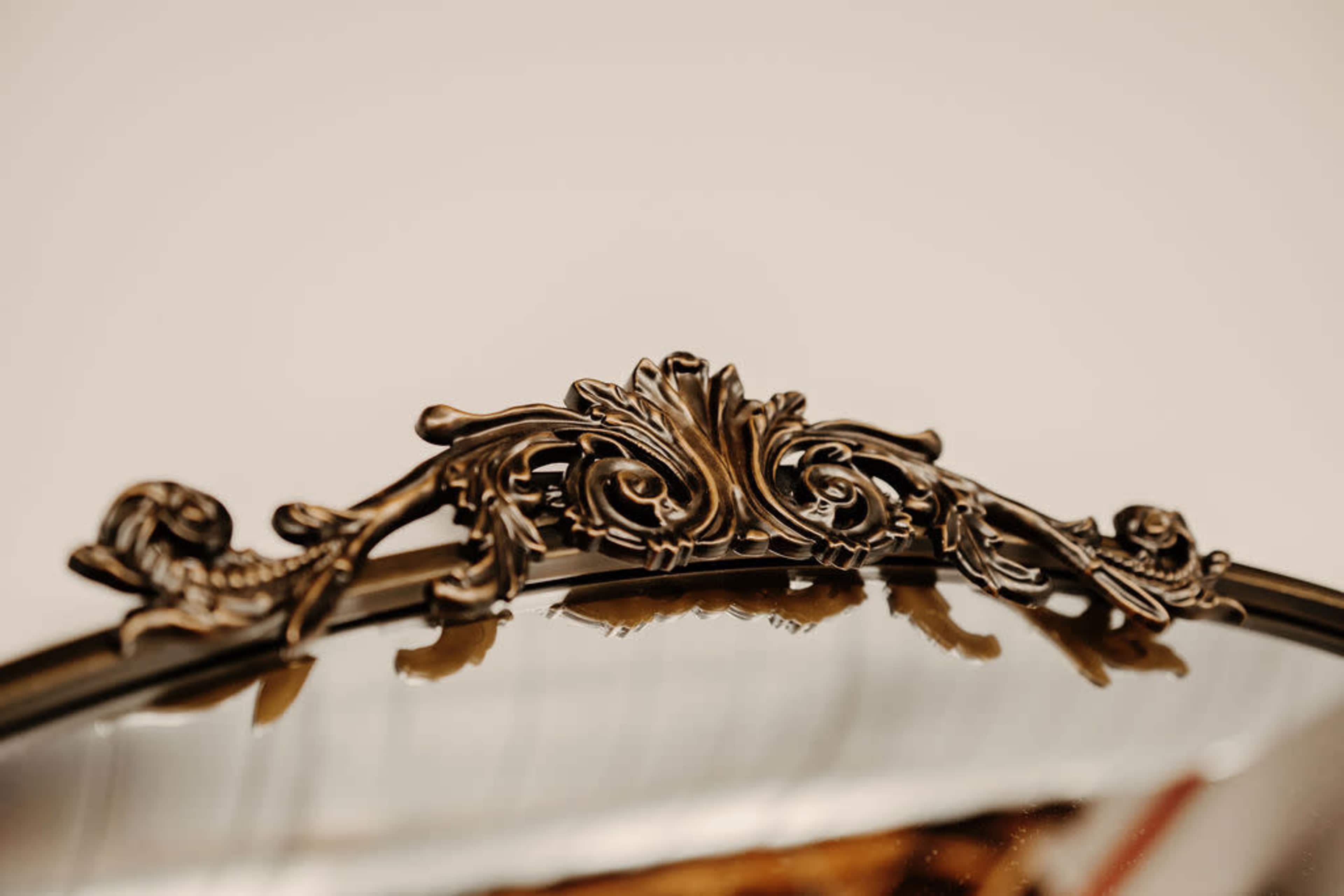 The image shows a decorative mirror featuring an ornate, vintage-style frame with intricate floral detailing at the top.