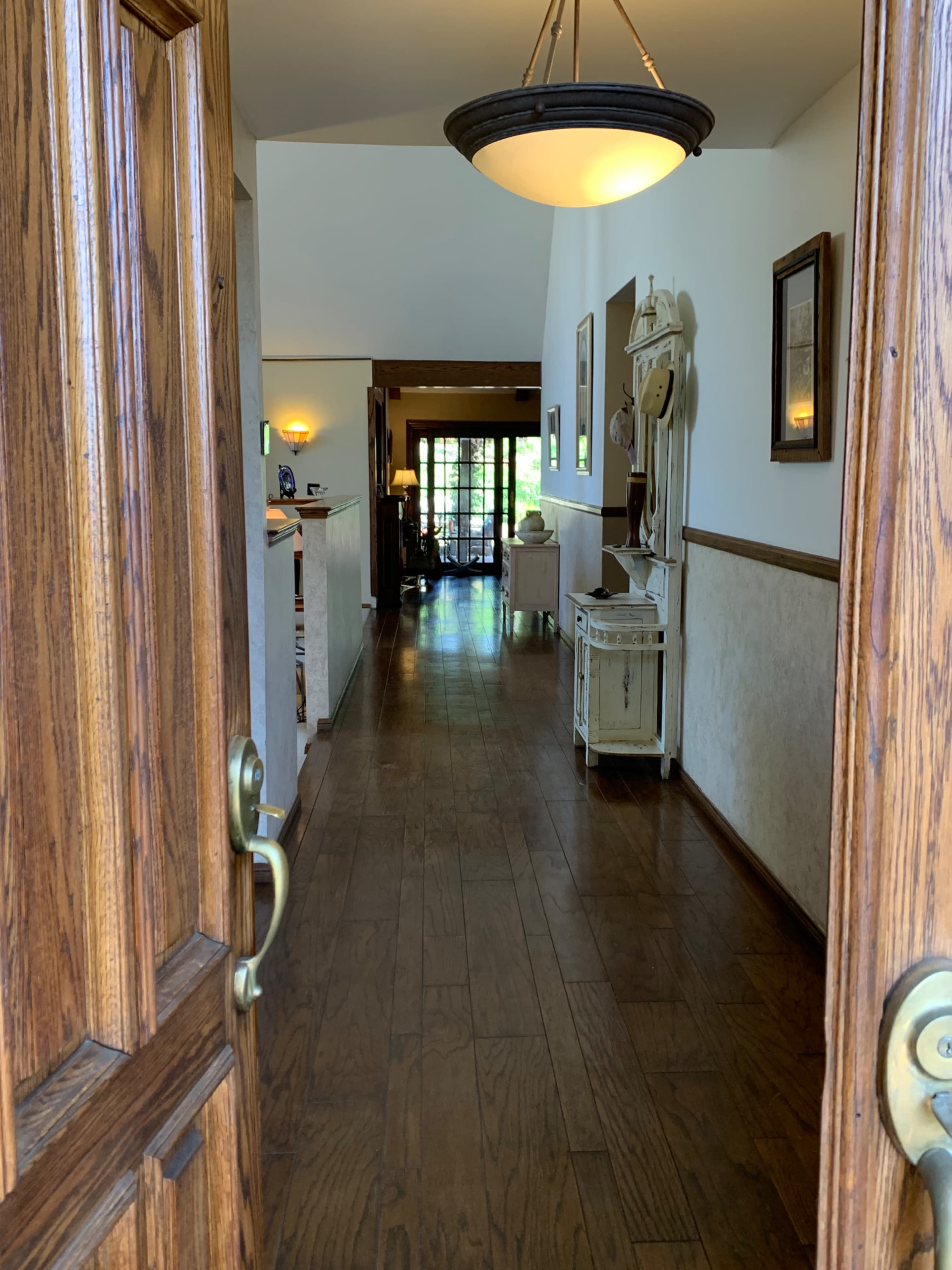 A wooden door opens to a hallway lined with framed pictures and wooden flooring, leading to a bright room at the end.