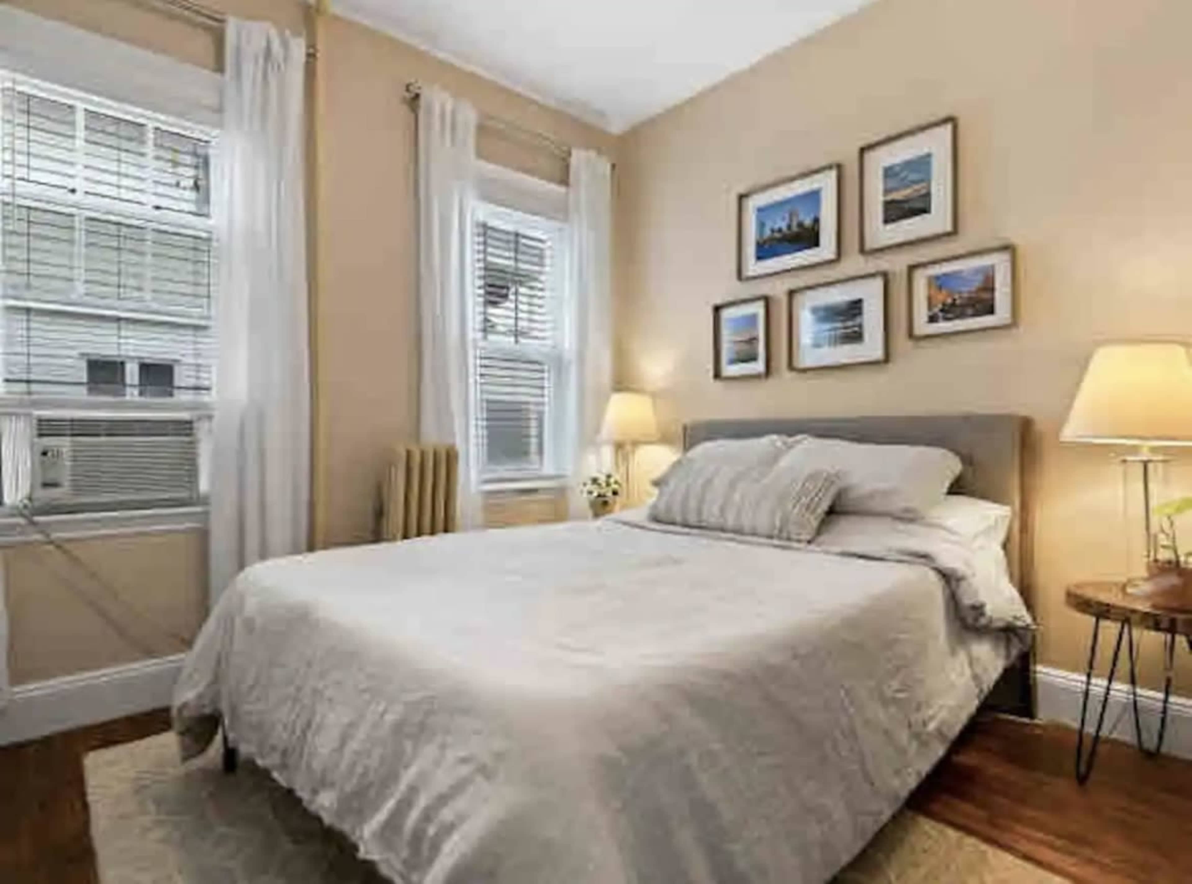 A neatly arranged bedroom with a bed, two bedside lamps, and framed pictures on the walls.