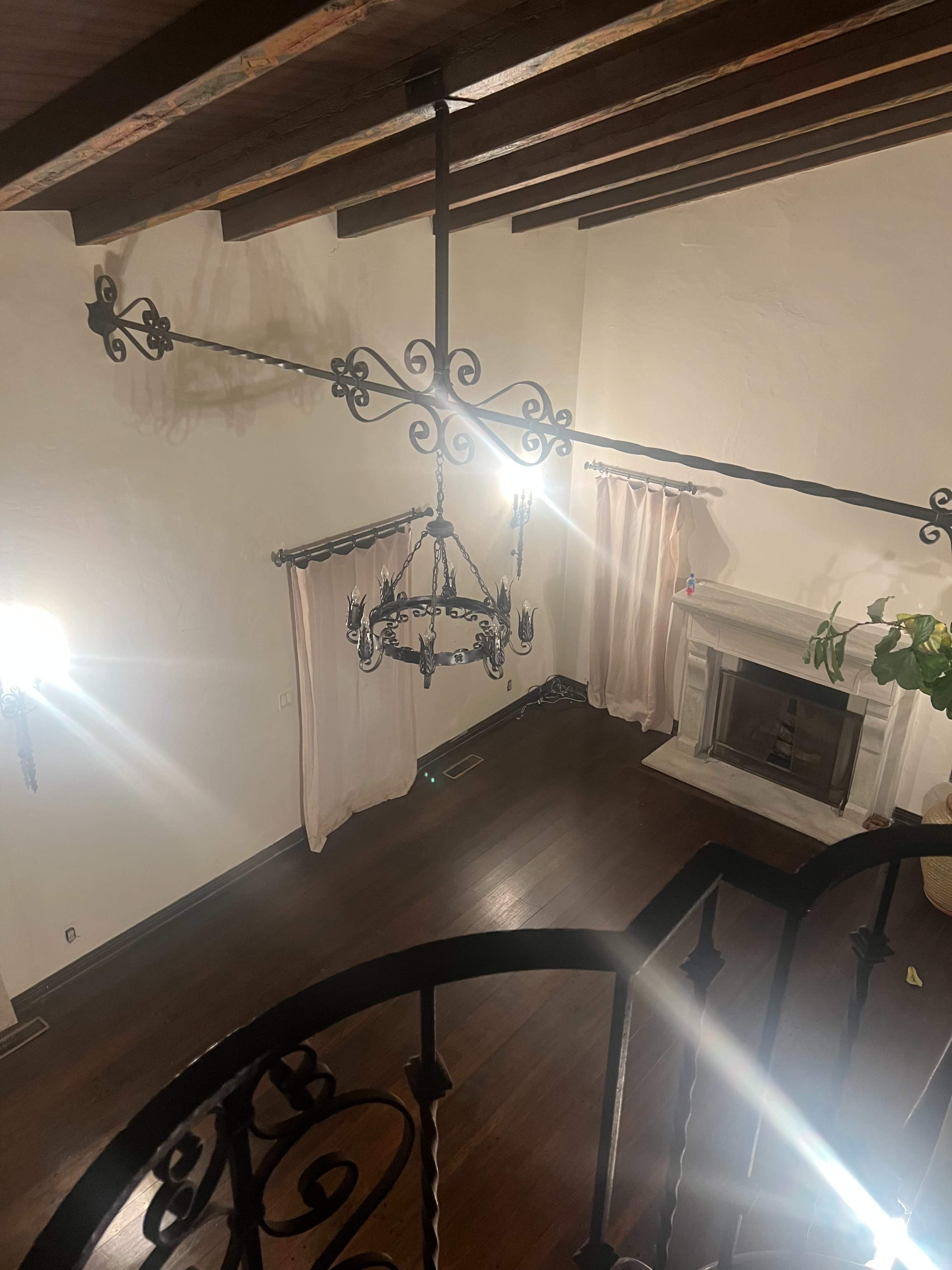 The image shows a room with high ceilings, featuring a chandelier, a fireplace, and large windows with drapes.