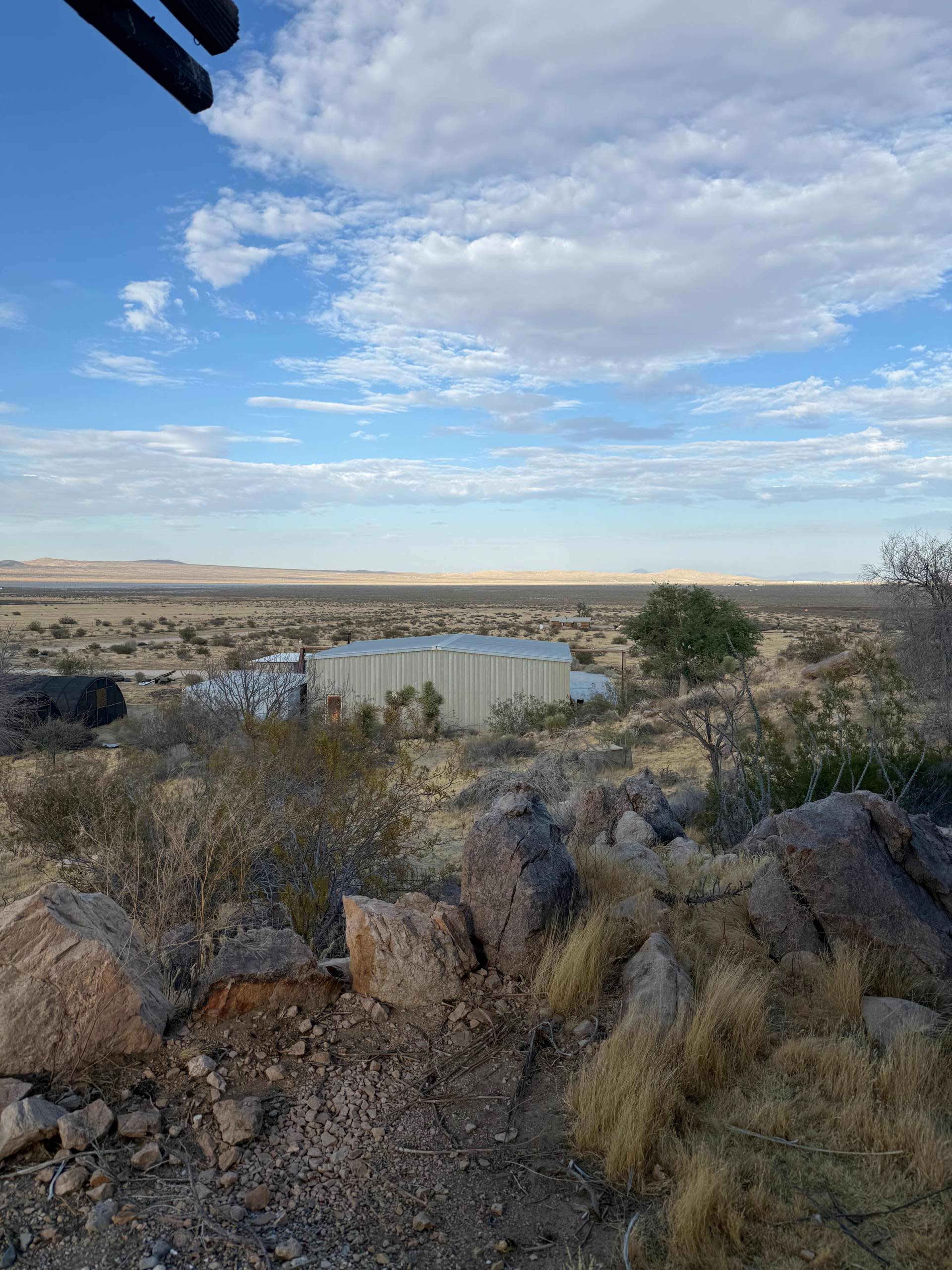 The image shows a metal structure in a sparse desert landscape with rocky terrain and a cloudy sky.