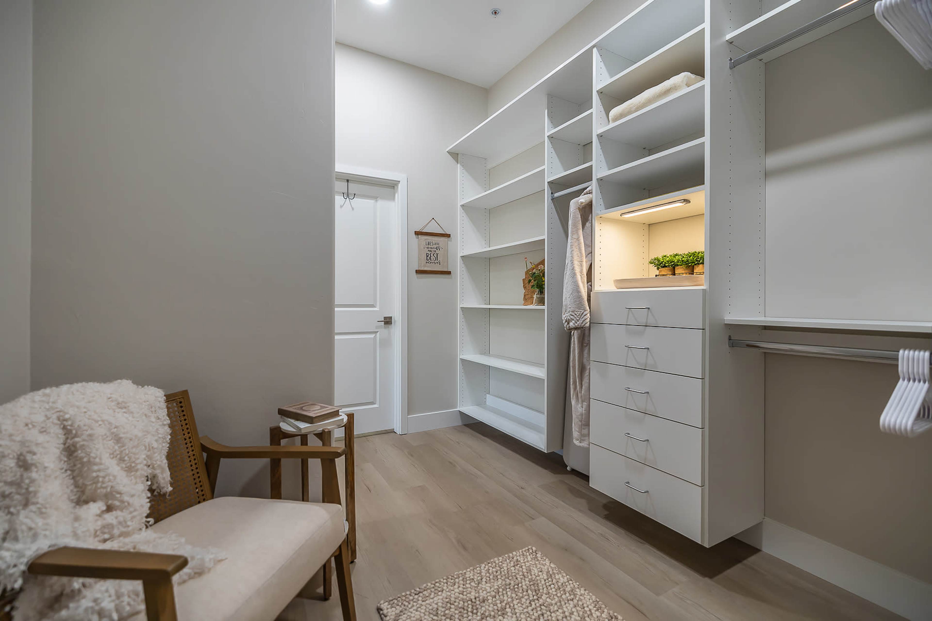 A neatly organized walk-in closet with white shelving, a chair, and soft lighting.