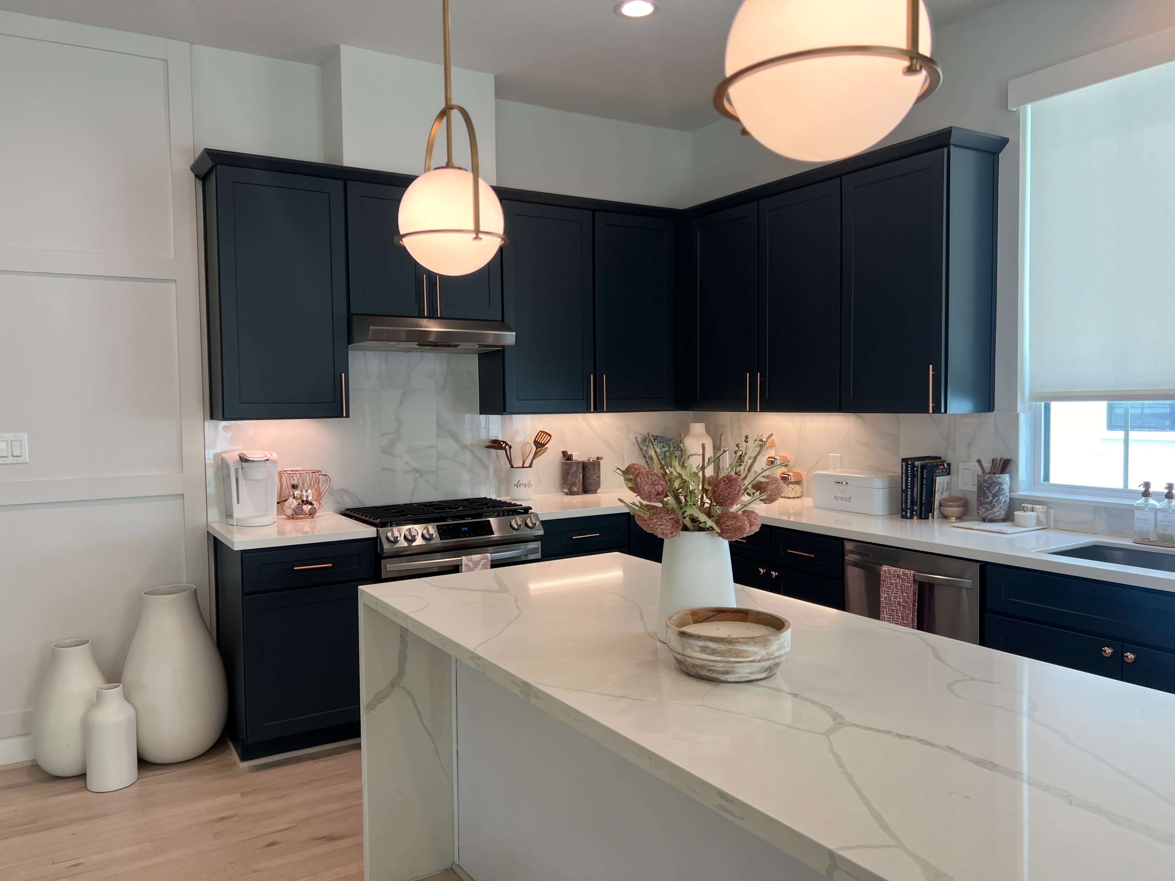 A modern kitchen features dark cabinetry, a marble island, and pendant lighting.