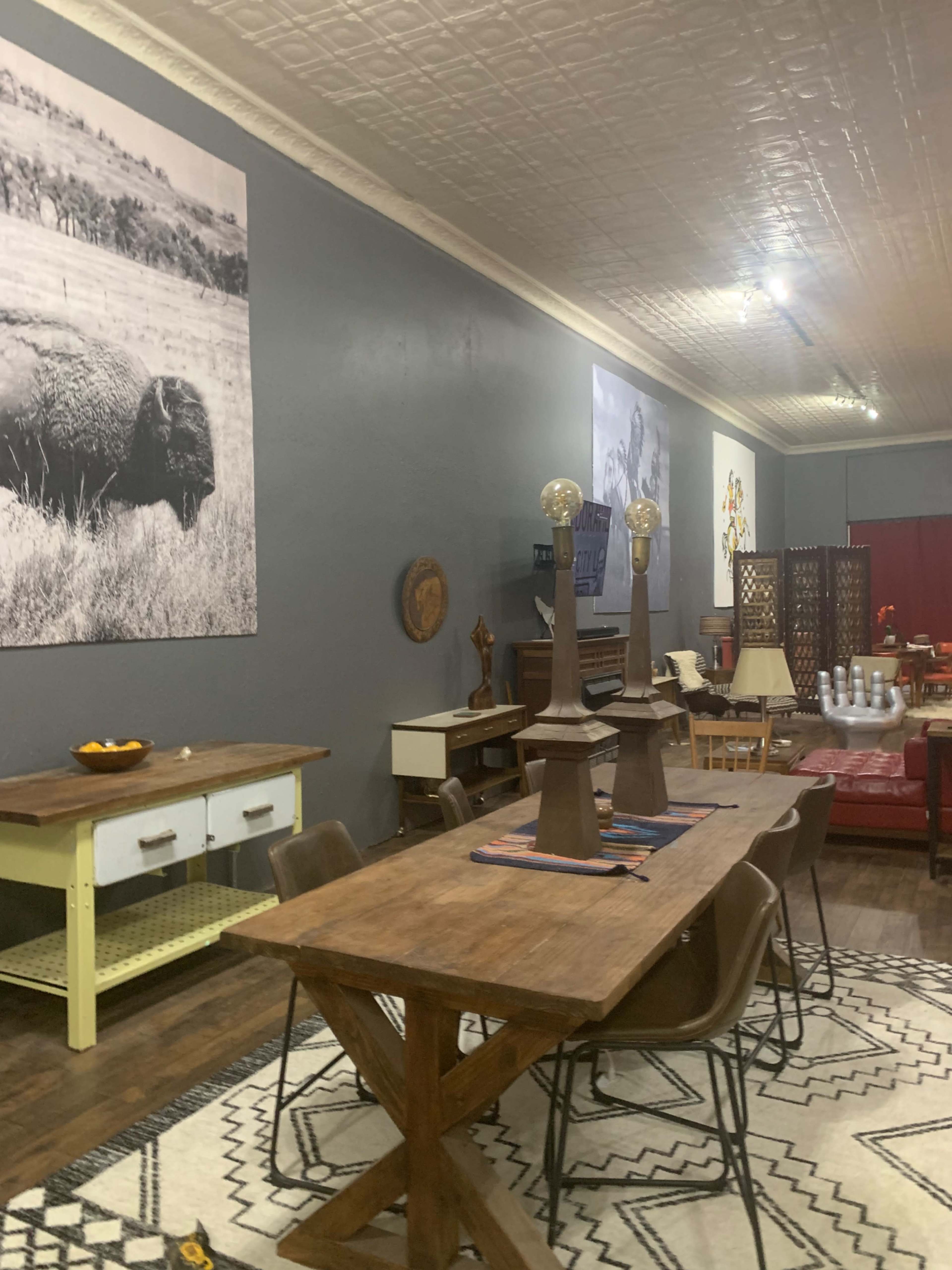 A spacious indoor area with a wooden dining table surrounded by chairs, large black-and-white photographs on the gray walls, and a mix of furniture items, including a piano and a decorative screen.