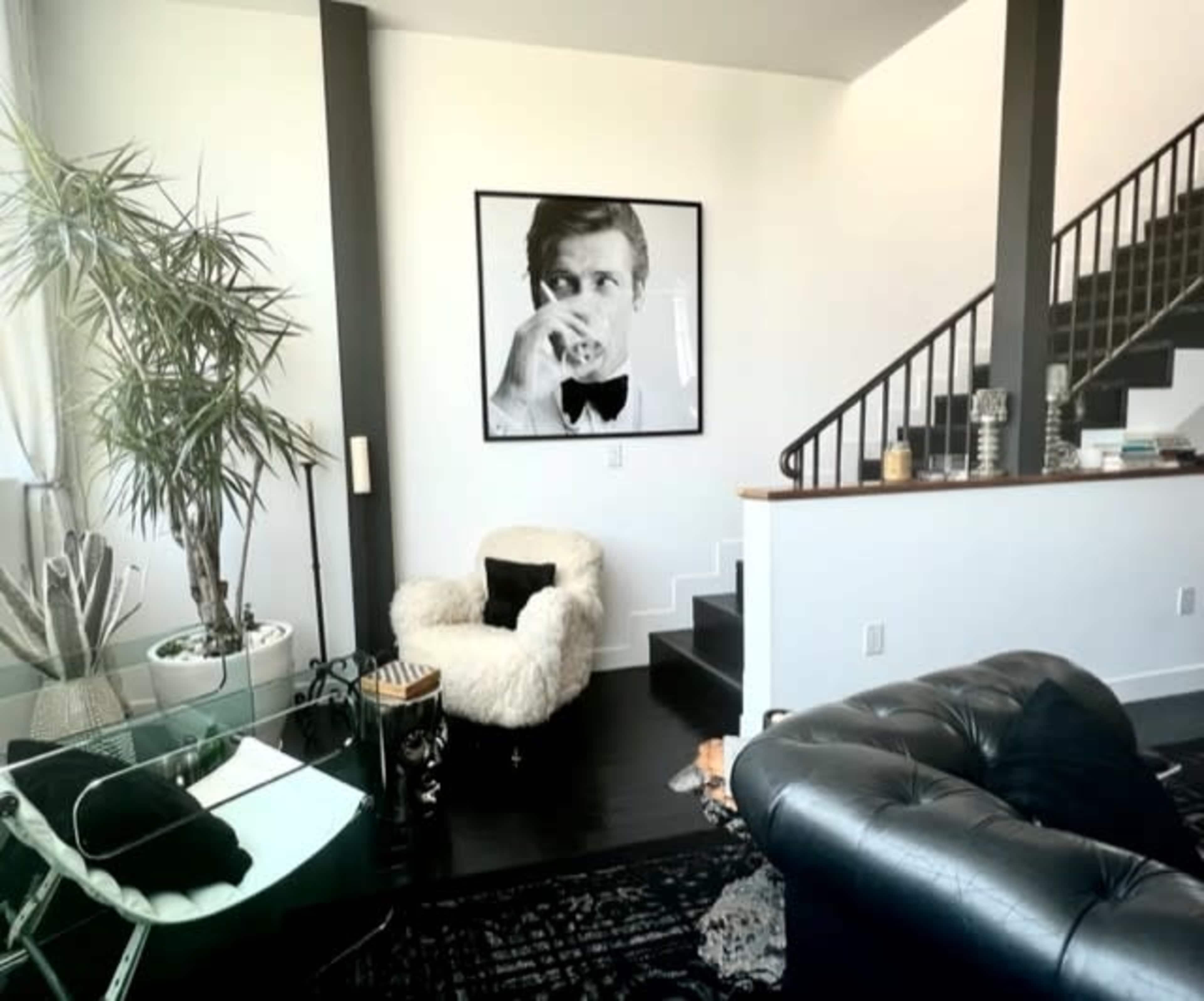 A modern living space features a large black and white portrait on the wall, accompanied by a fur armchair, a glass table, and a staircase.