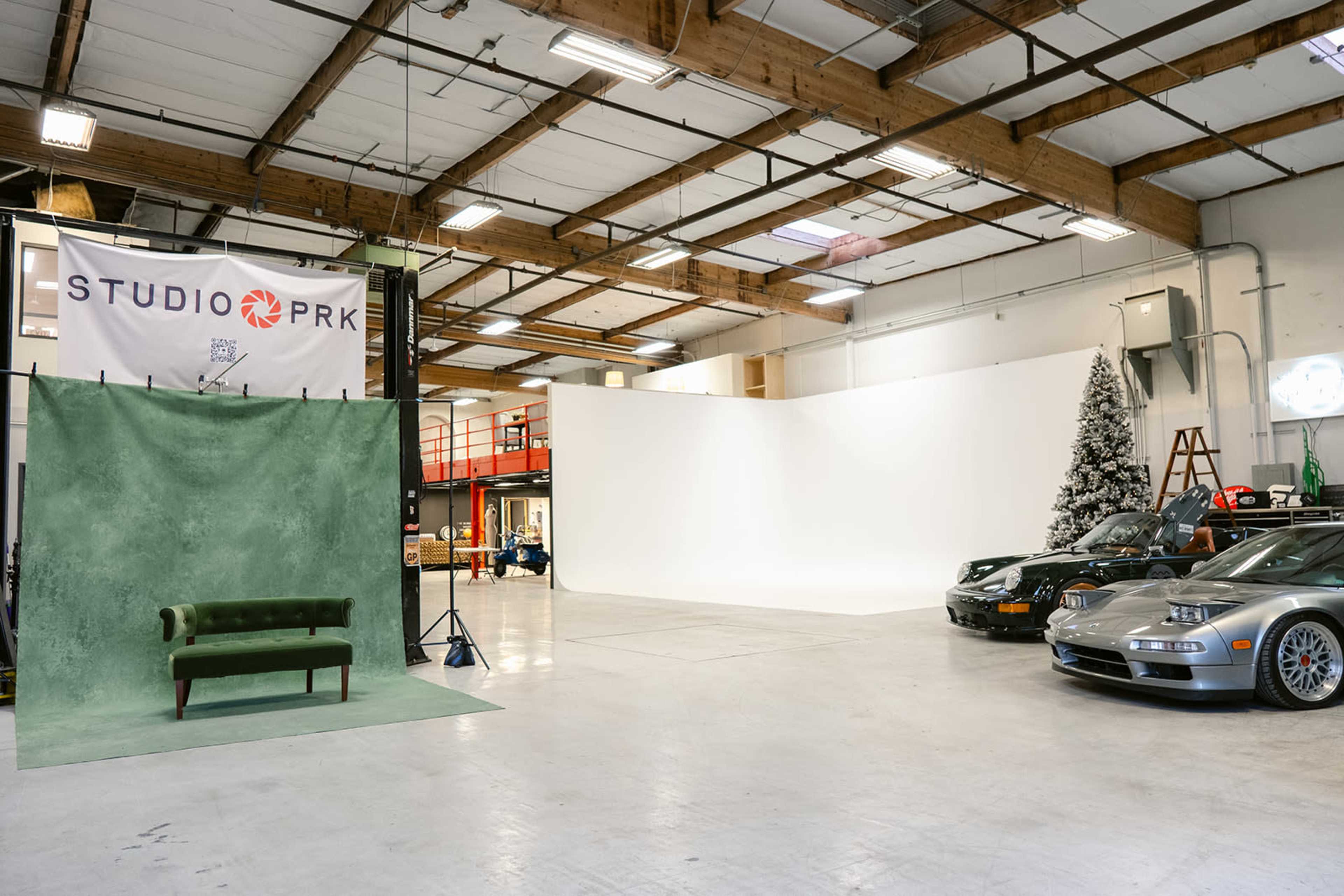 The image shows a spacious studio interior featuring a green backdrop, a couch, and several cars parked nearby, along with a Christmas tree in the corner.