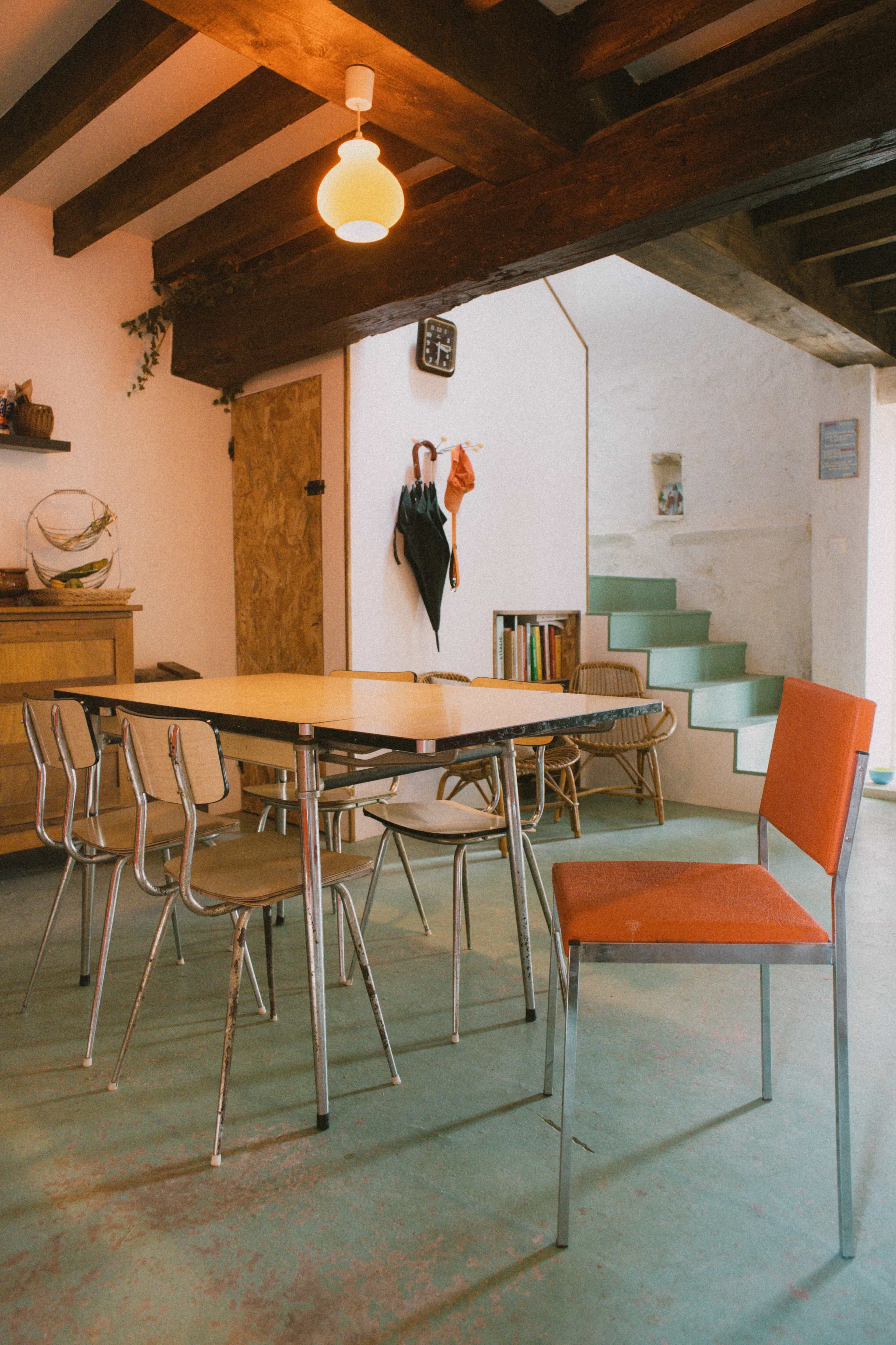 A modern dining area featuring a rectangular table surrounded by six metal chairs, with a staircase and various decorative elements in the background.