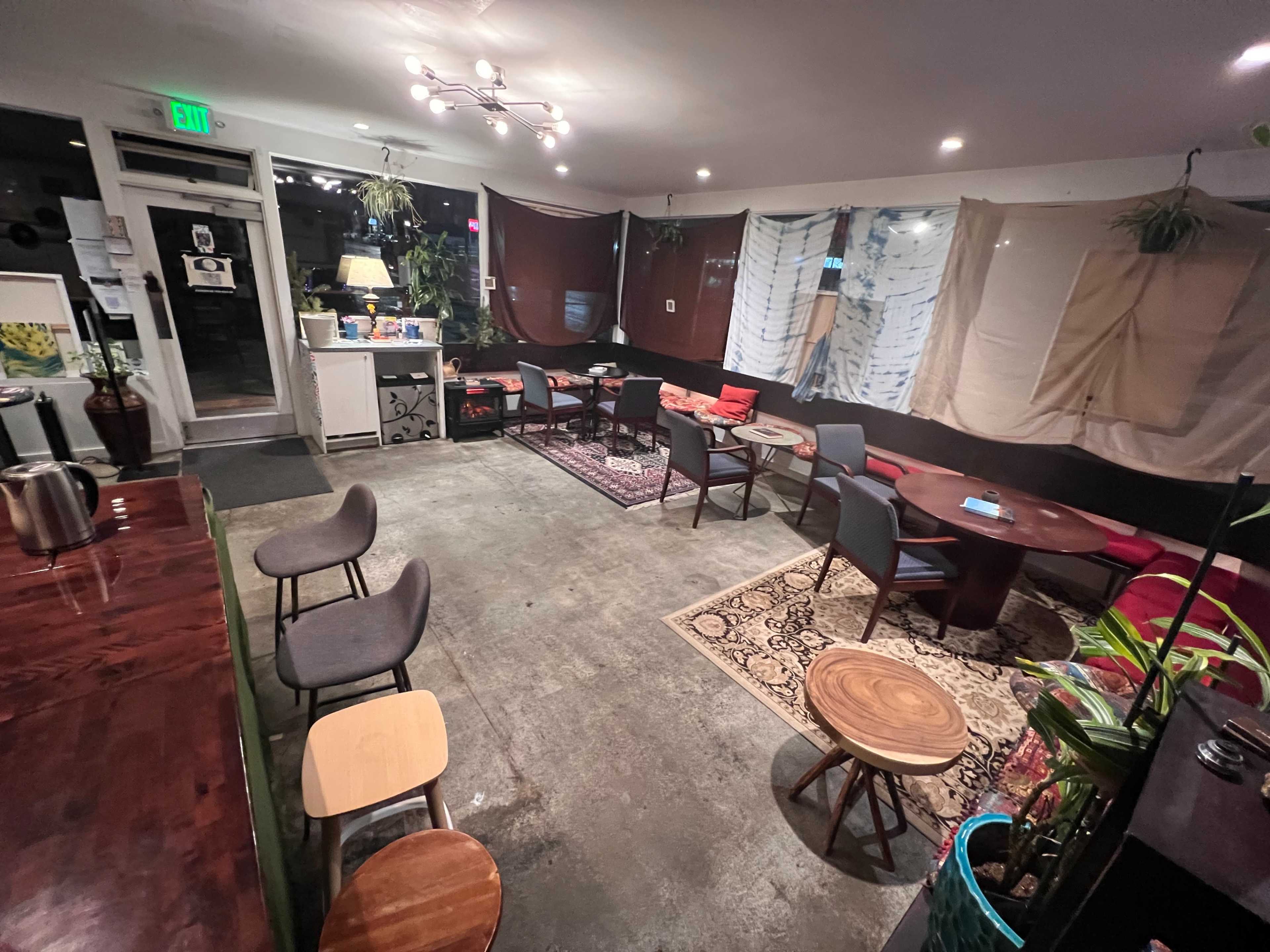 The image shows a cozy café interior with assorted tables and chairs, dim lighting, and partially draped windows.