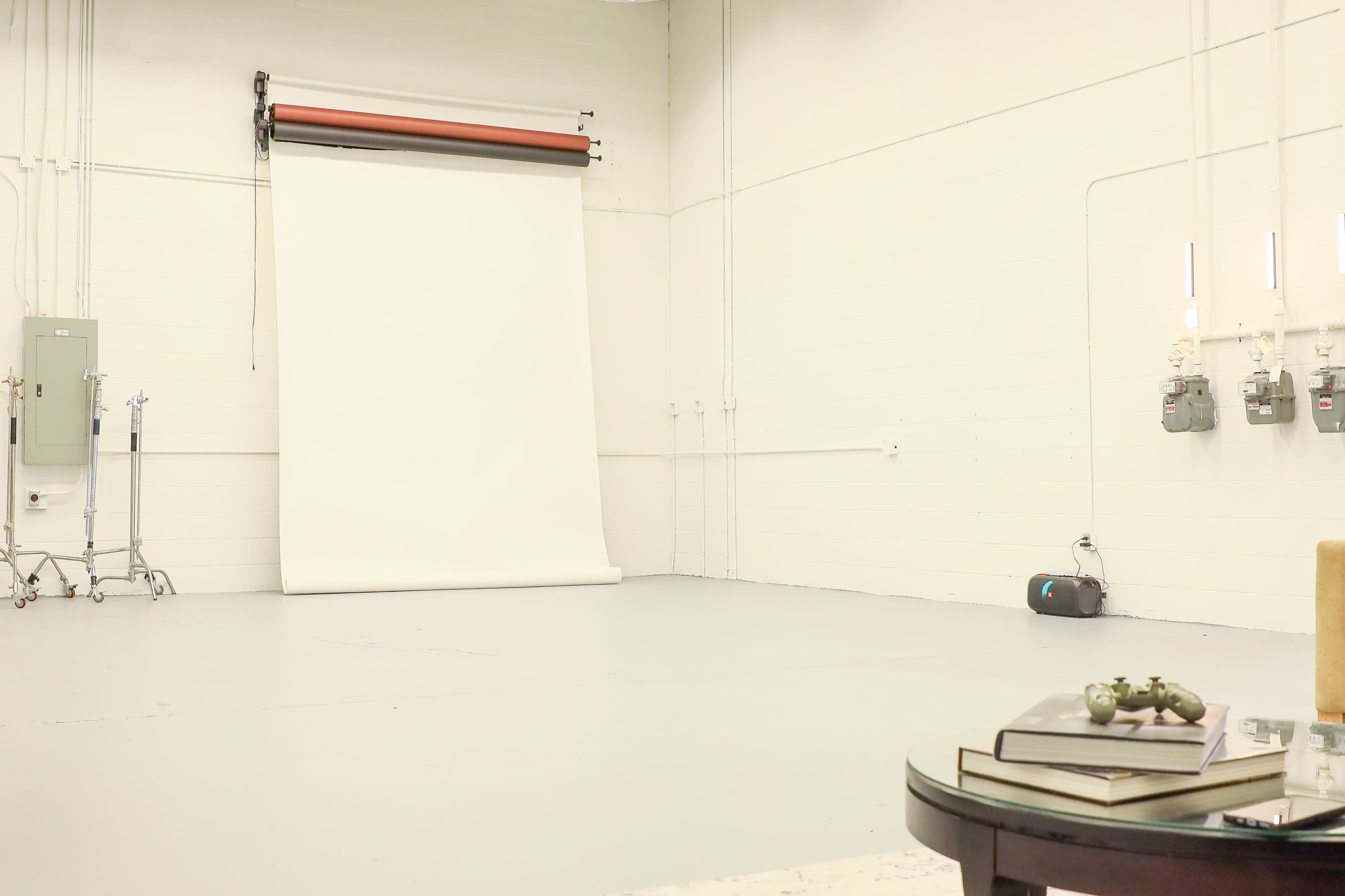 A spacious, empty studio with a white backdrop and minimal furnishings, including a round table and a small decorative item.