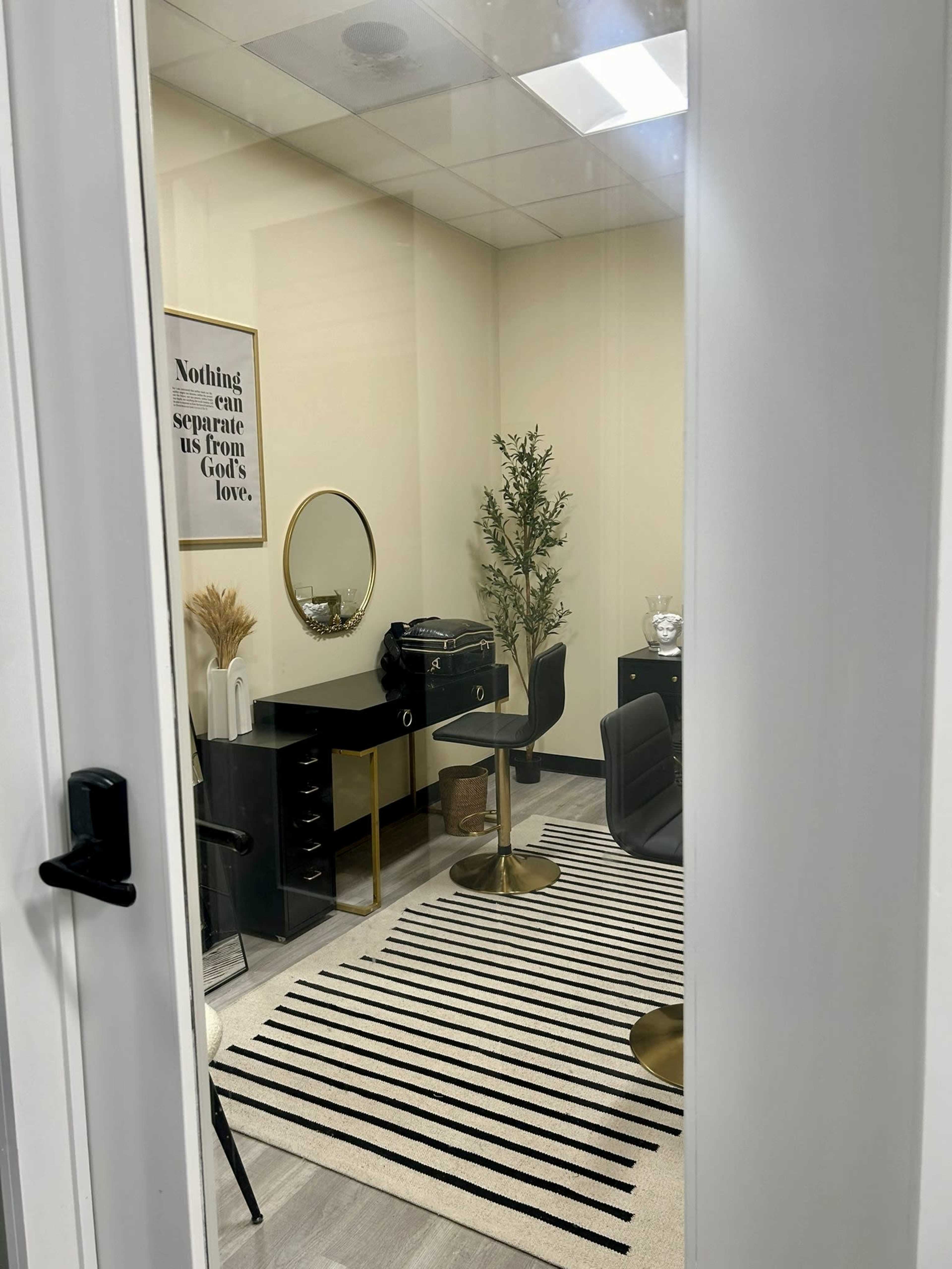 A small office space with a black desk, chairs, a round mirror, and decorative elements, all visible through a glass door.