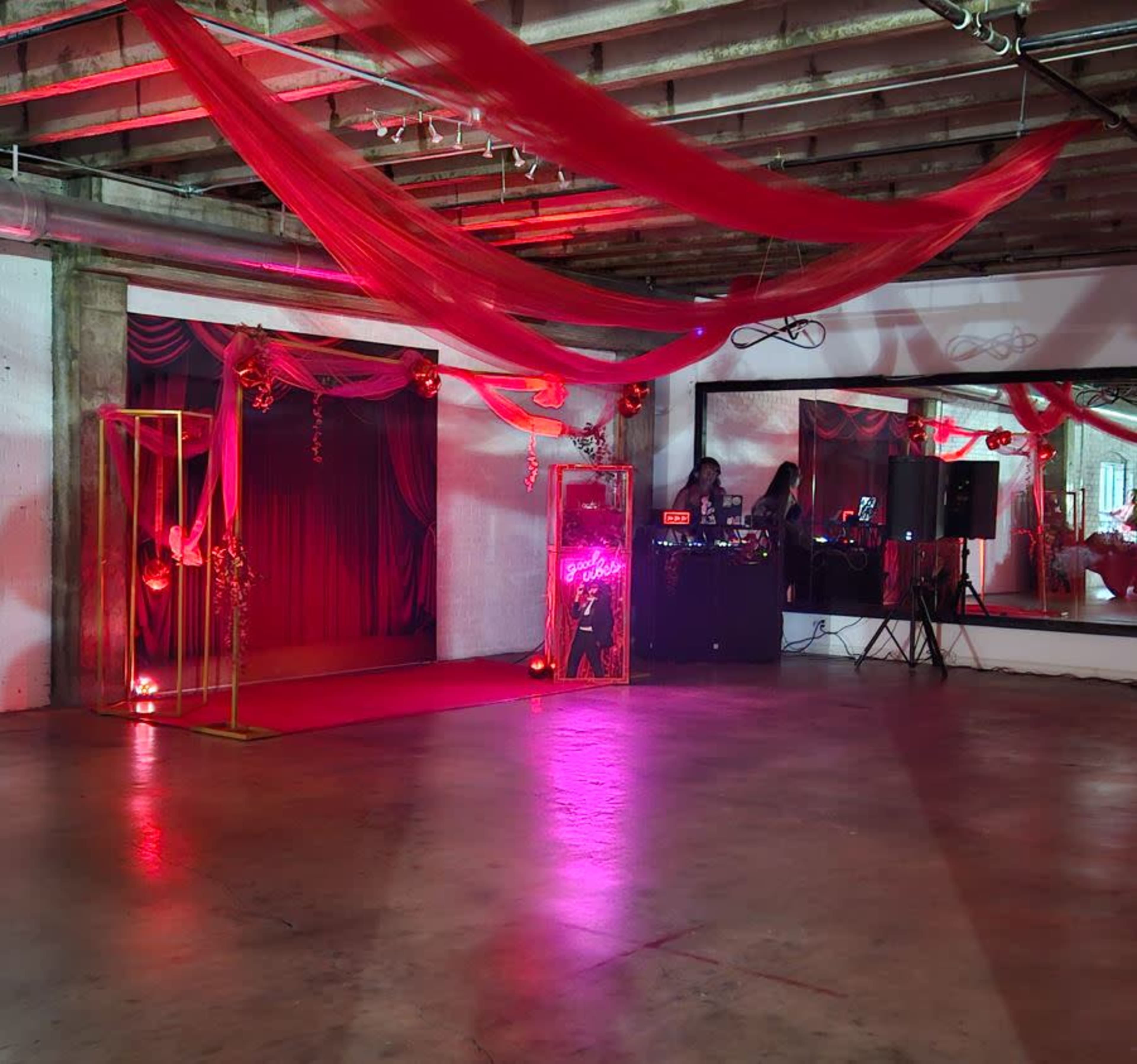 The image shows an event space featuring a decorated stage area with draped fabric, a DJ setup, and mirrored walls.