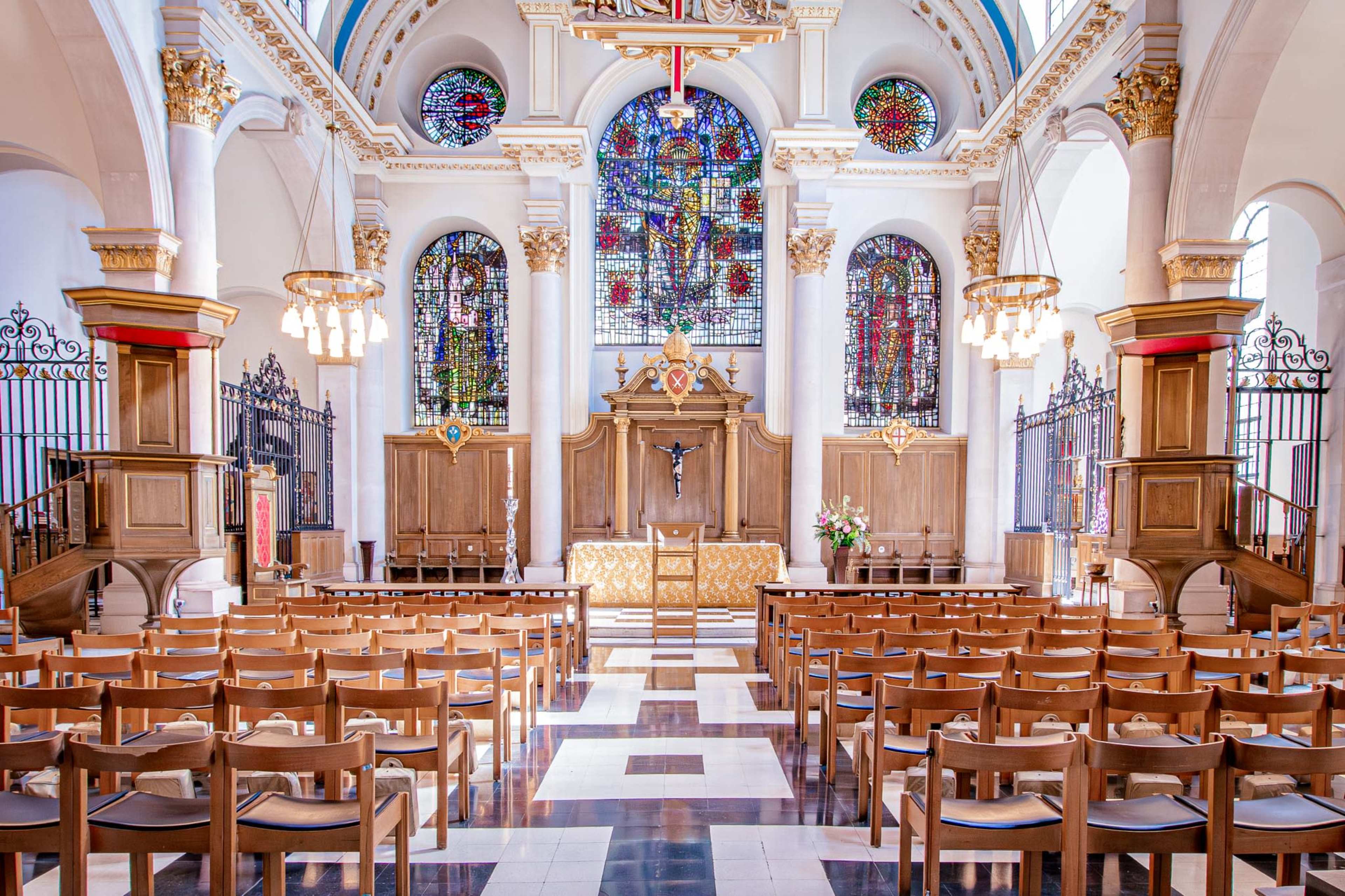The image shows the interior of a church featuring wooden pews, a raised altar, and large stained glass windows.